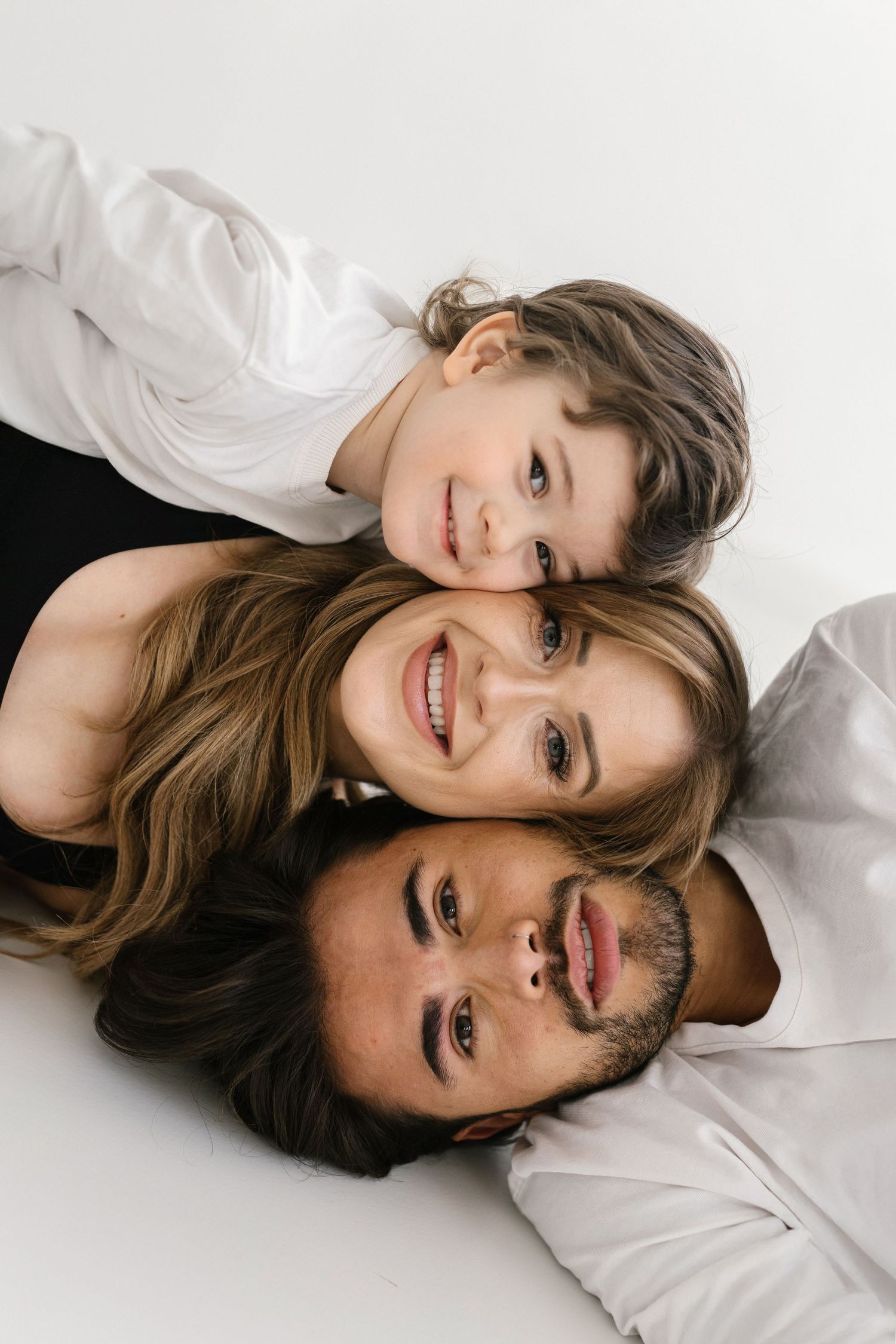 Couple in white shirts lying down for romantic studio photoshoot against white background.
