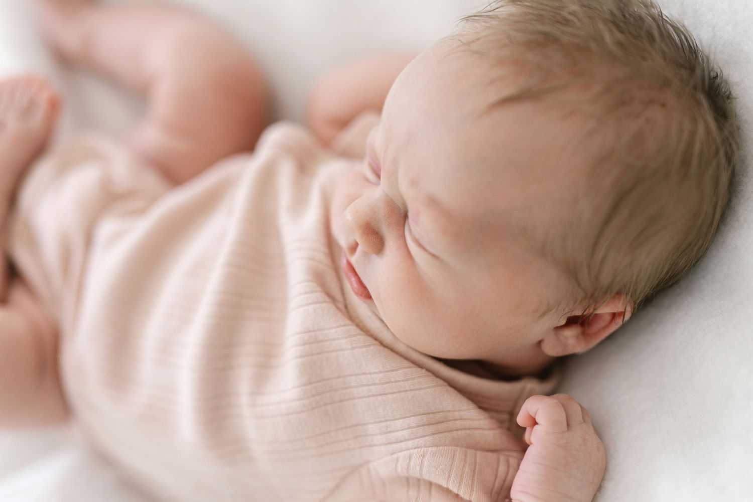 A peaceful newborn baby sleeping in a soft pink onesie on a white blanket.