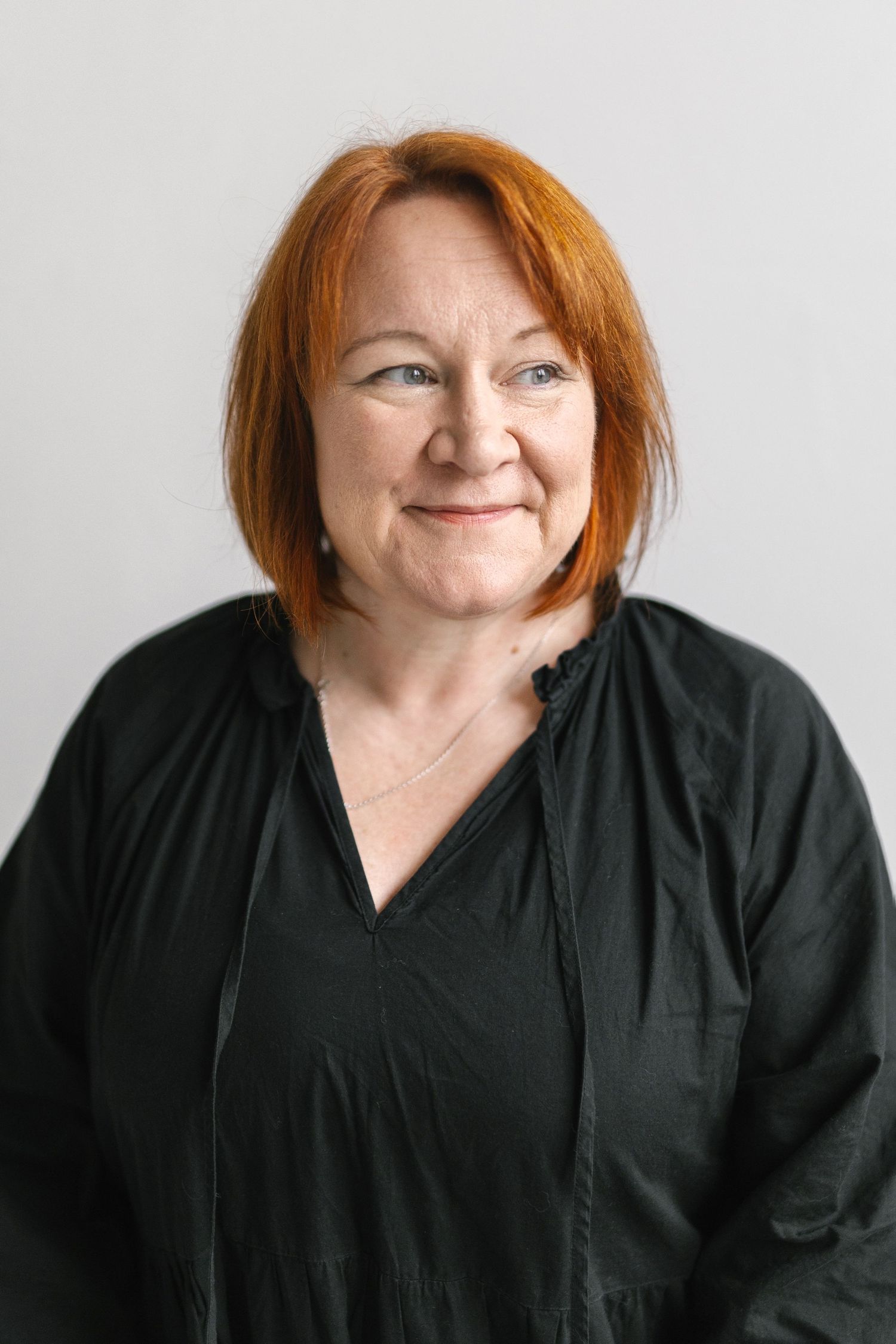 Portrait of person with red hair wearing black top against neutral background.