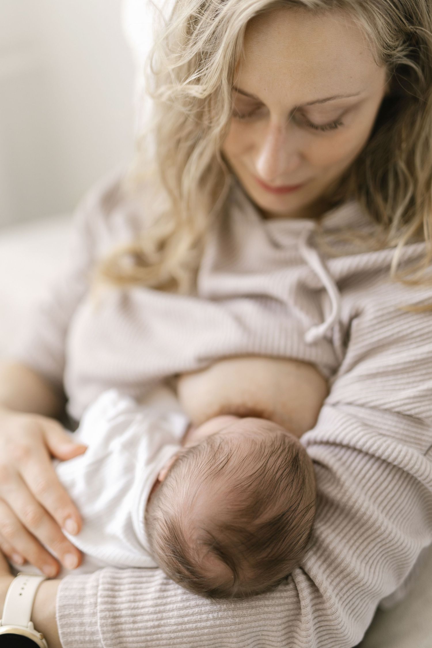 A tender moment as a newborn baby rests against a soft beige sweater while being cradled.