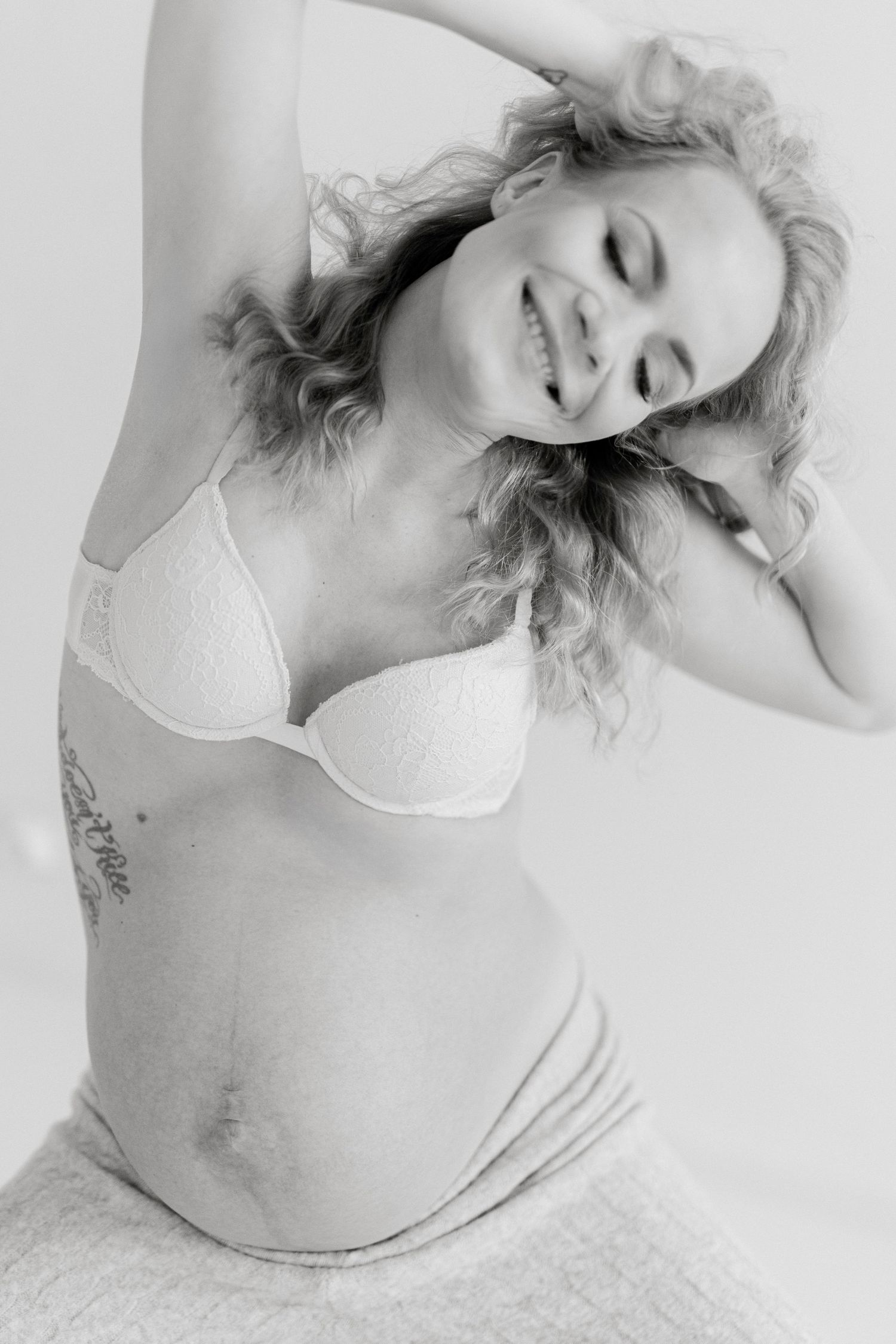 Black and white artistic maternity portrait showing joyful expression and natural curves.