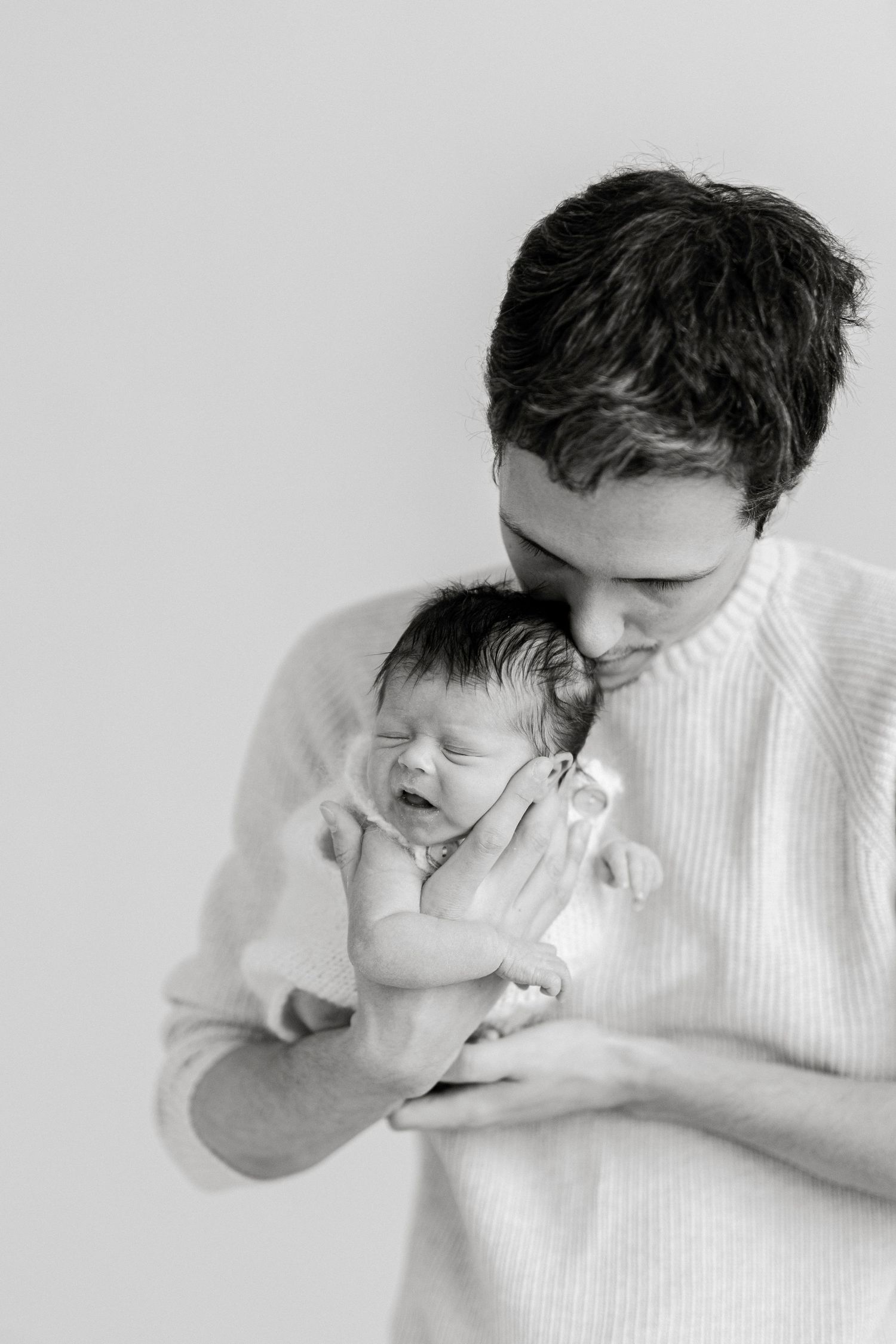 Tender moment between parent and newborn in soft black and white photography.