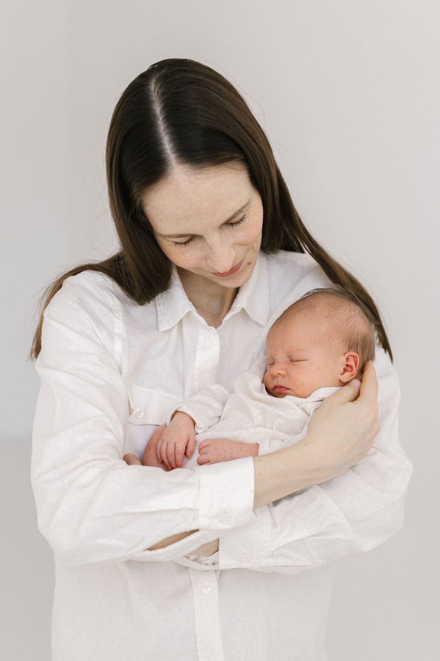 Parent in white shirt holding sleeping newborn baby in minimalist portrait series.
