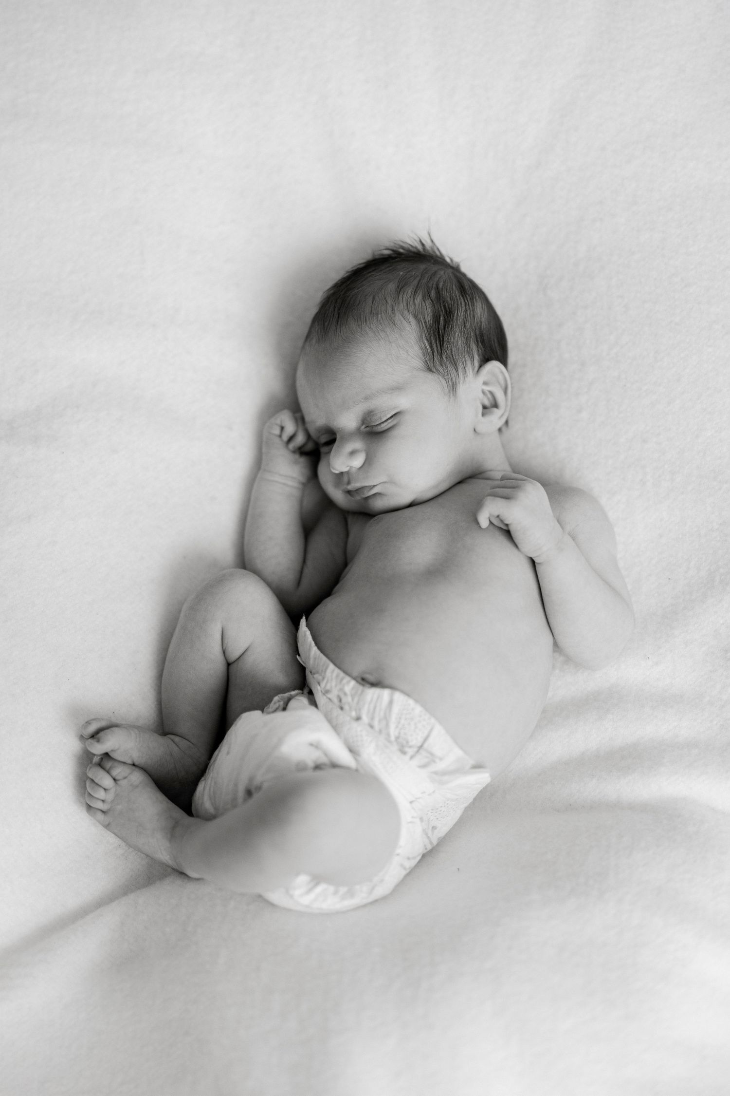 Black and white photo of a peaceful sleeping newborn baby in a diaper on a soft white blanket.