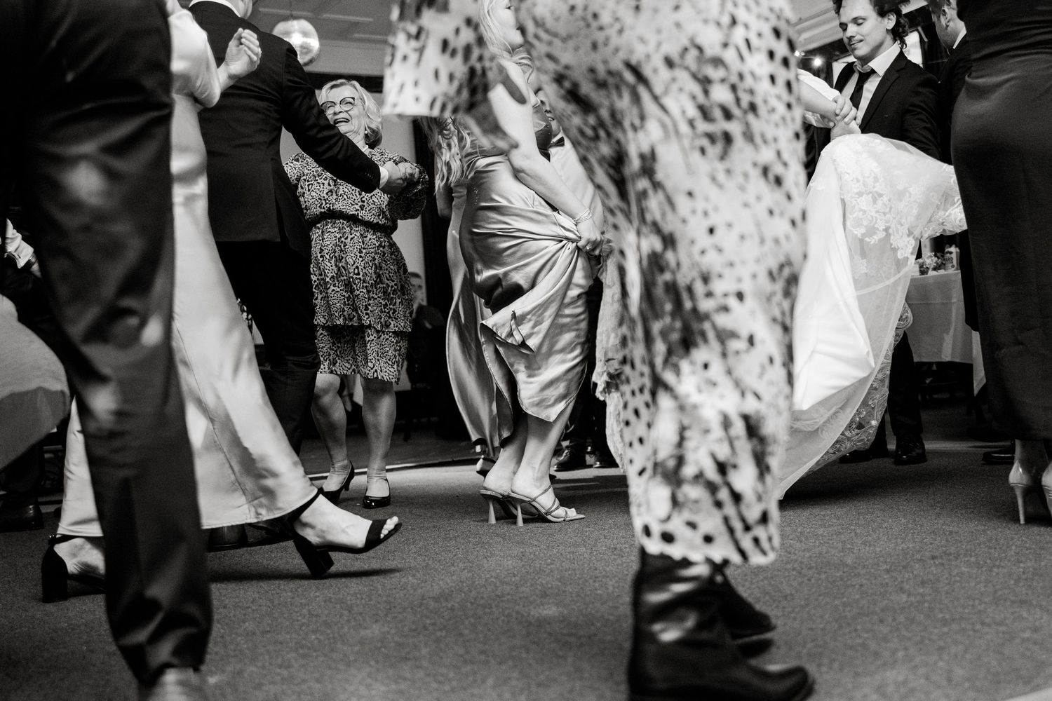 Low angle black and white shot of dancing feet and formal wear at a wedding reception.