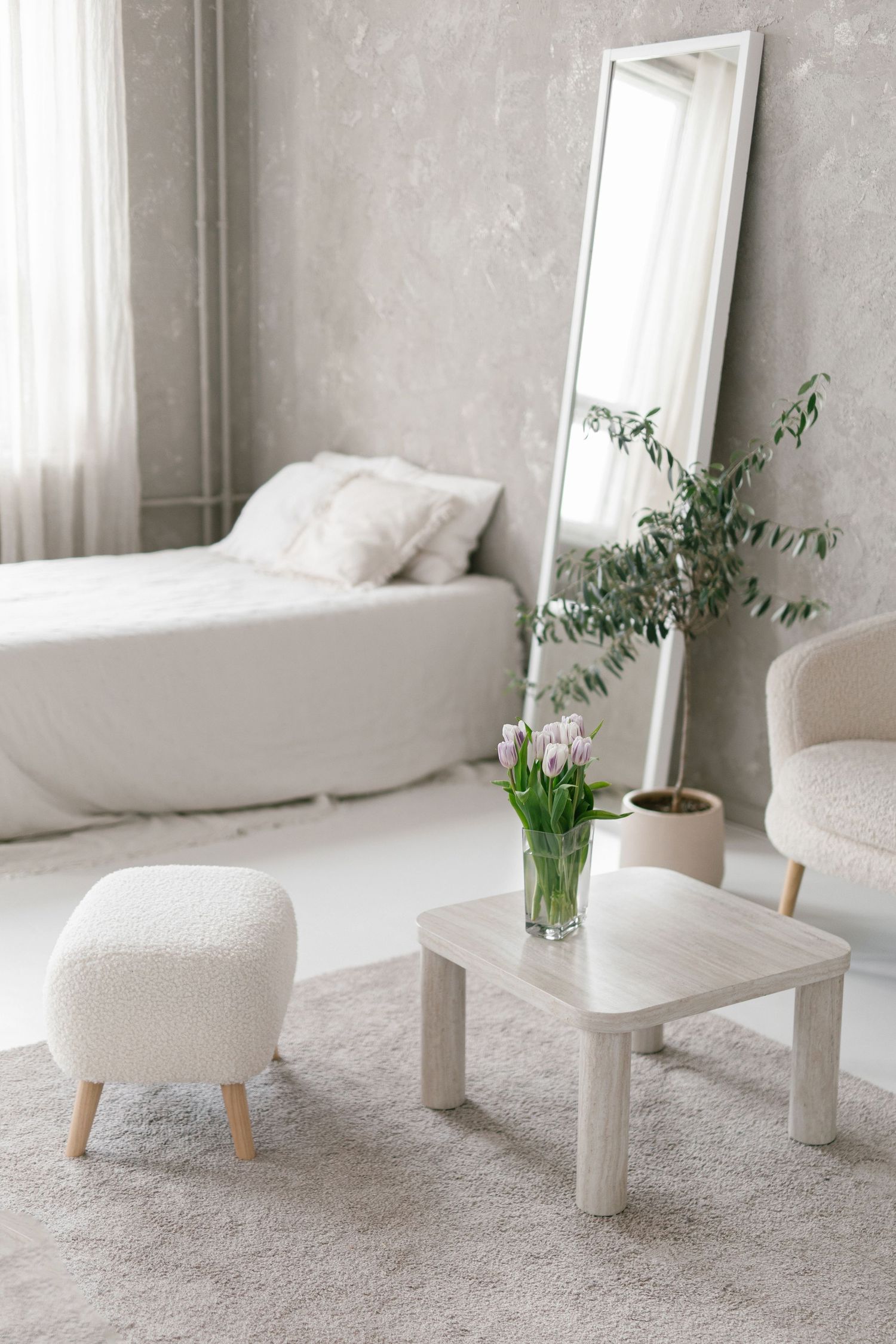 Minimalist white interior design featuring a cozy armchair, side table, and potted plants by a bright window.