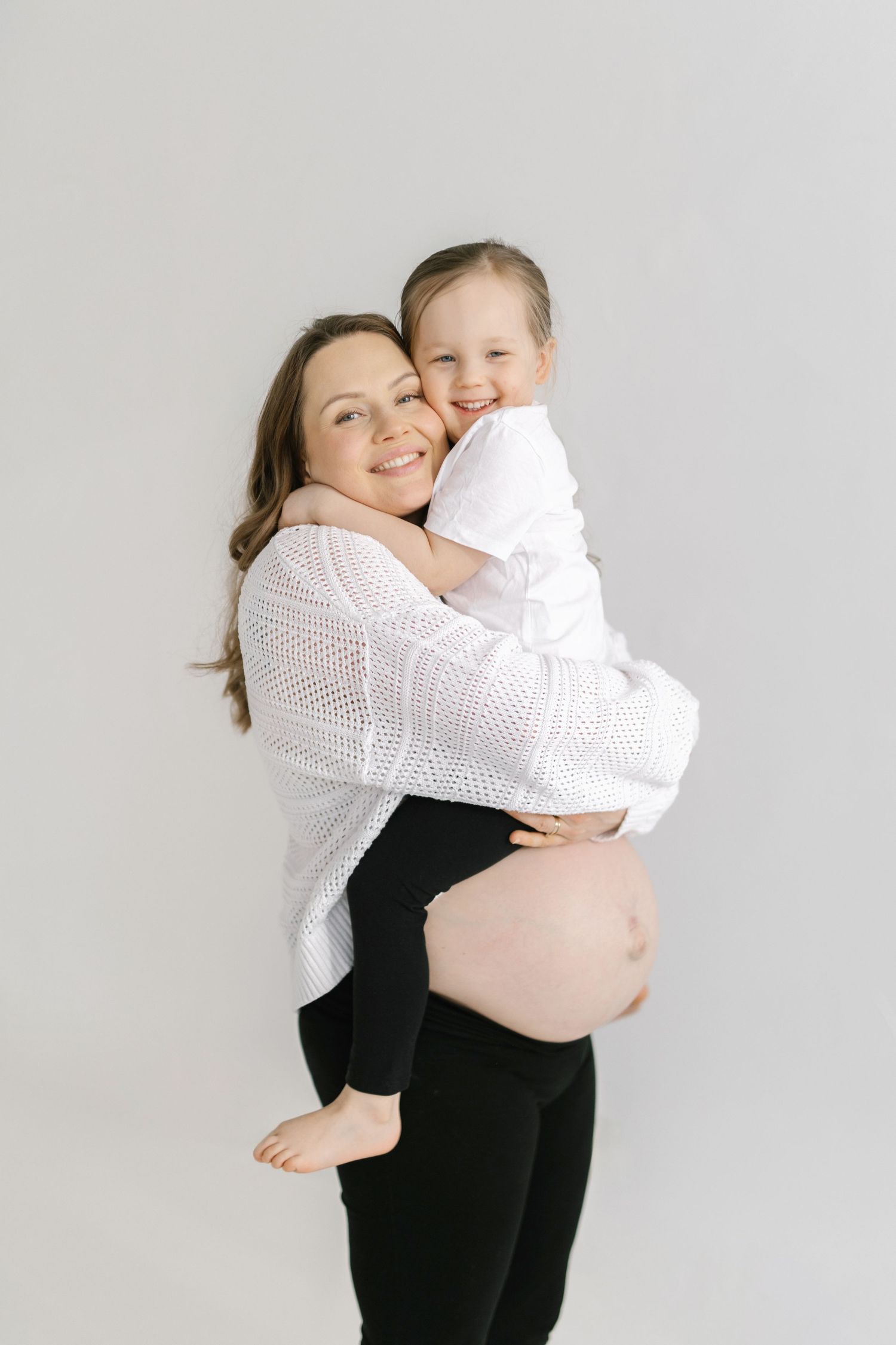 A tender moment captured in black and white as a woman in dark clothing embraces a baby wearing white.
