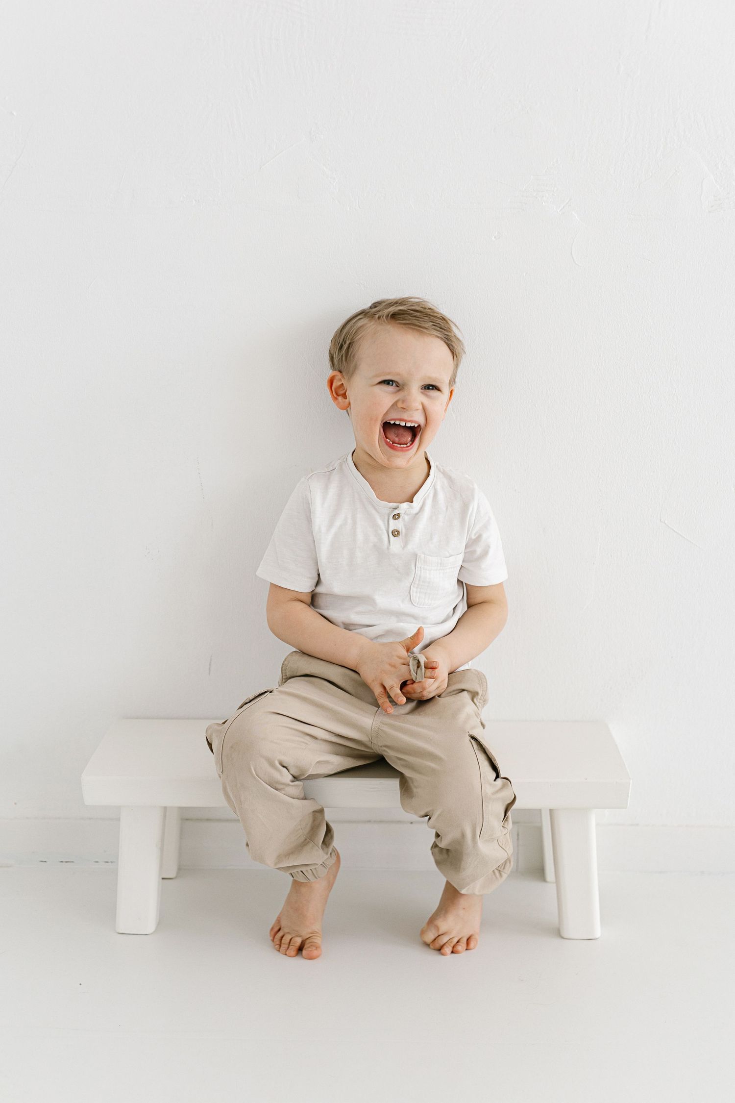 Three progressive photos show a toddler in white shirt and khaki pants sitting on a white bench with increasing expressions of joy.