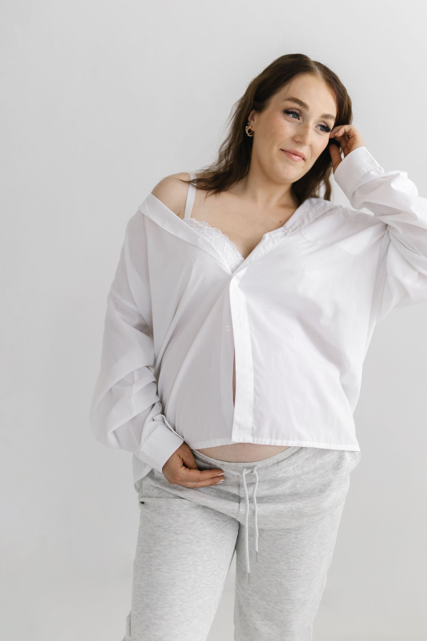 Woman in white button down shirt and gray sweatpants poses against white background.