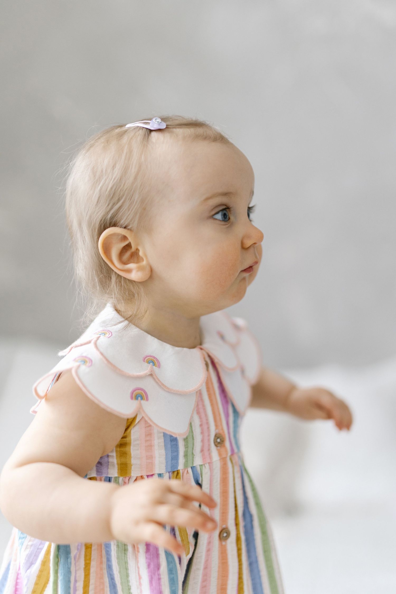 Baby in a rainbow striped dress crawling and exploring against a white background.