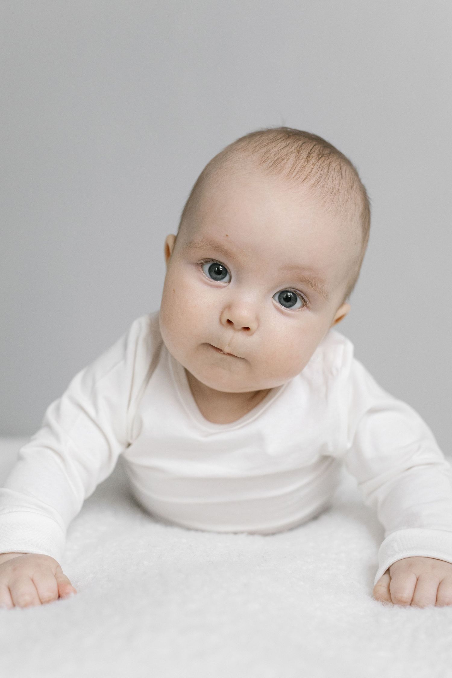 Baby in white turtleneck showing various expressions against light grey background.