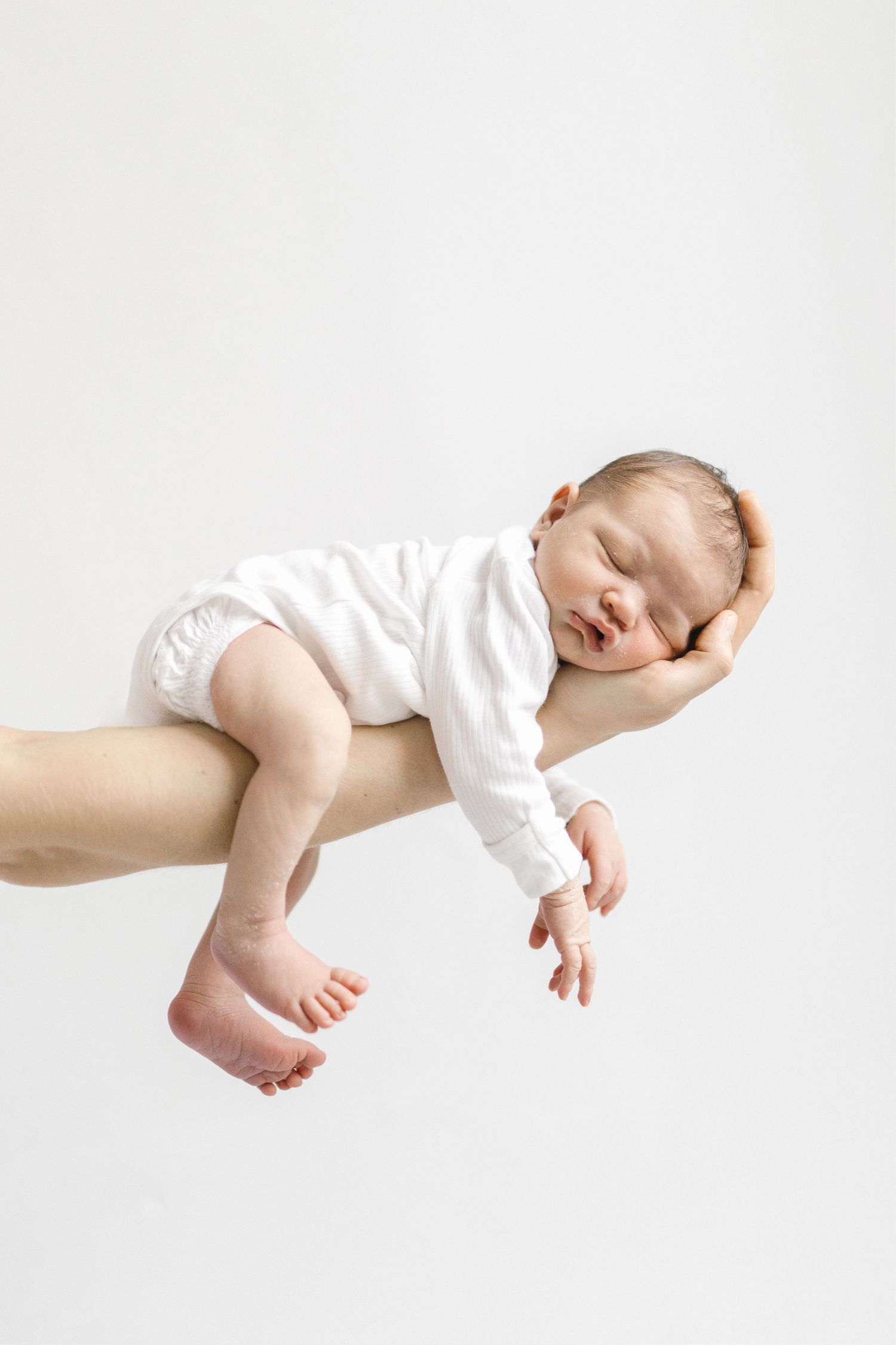 Baby in white onesie being held horizontally against white background showing peaceful sleeping poses.