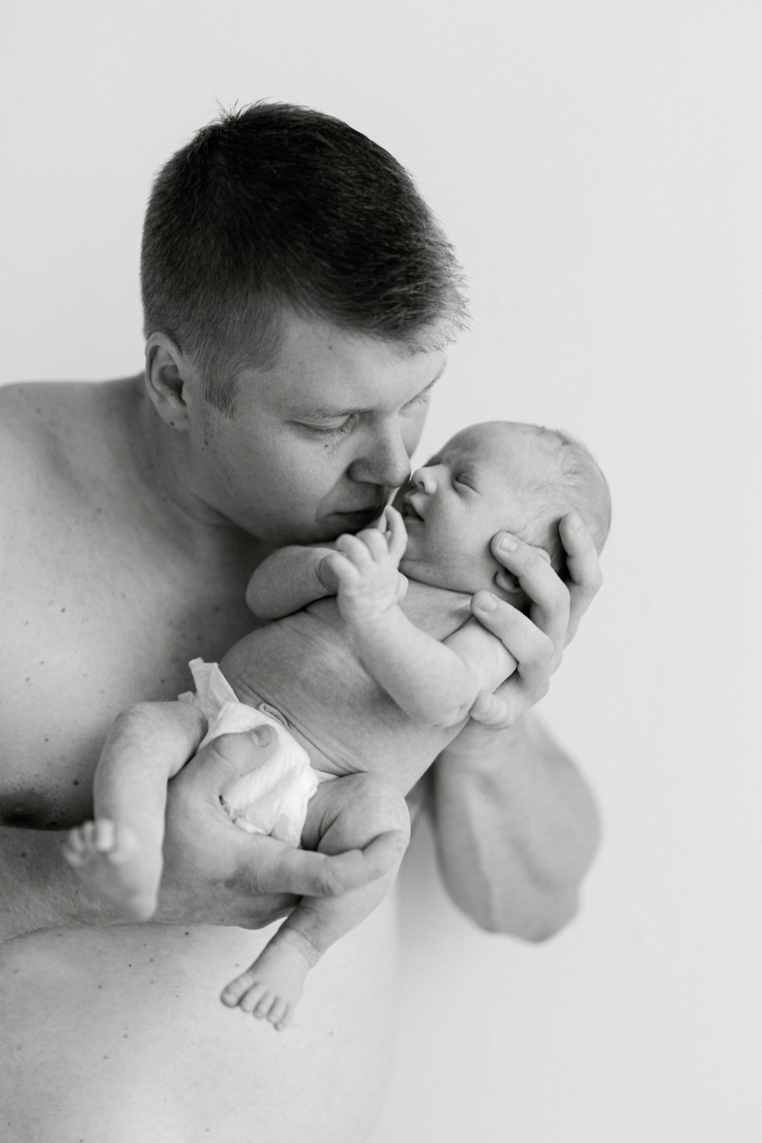 Black and white intimate portrait of a parent holding and nuzzling their newborn baby.