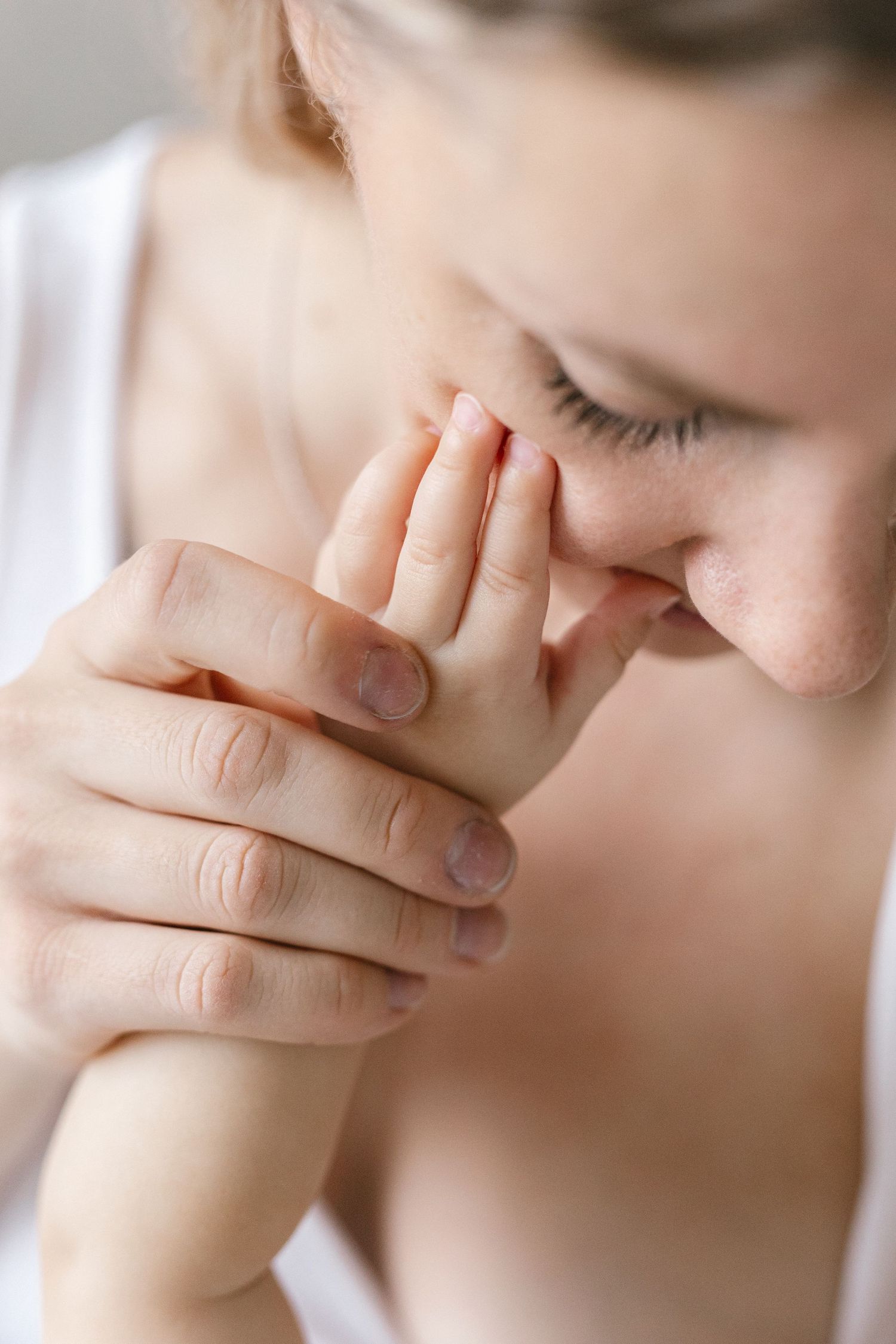 Close-up of a mother gently pressing her baby's tiny hand to her face with her eyes closed in a tender, loving moment.