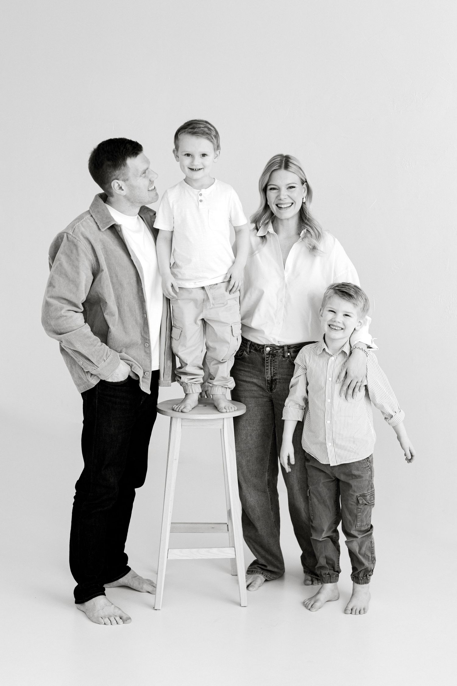Black and white family portrait of parents with two young boys, smiling in casual attire against white background.