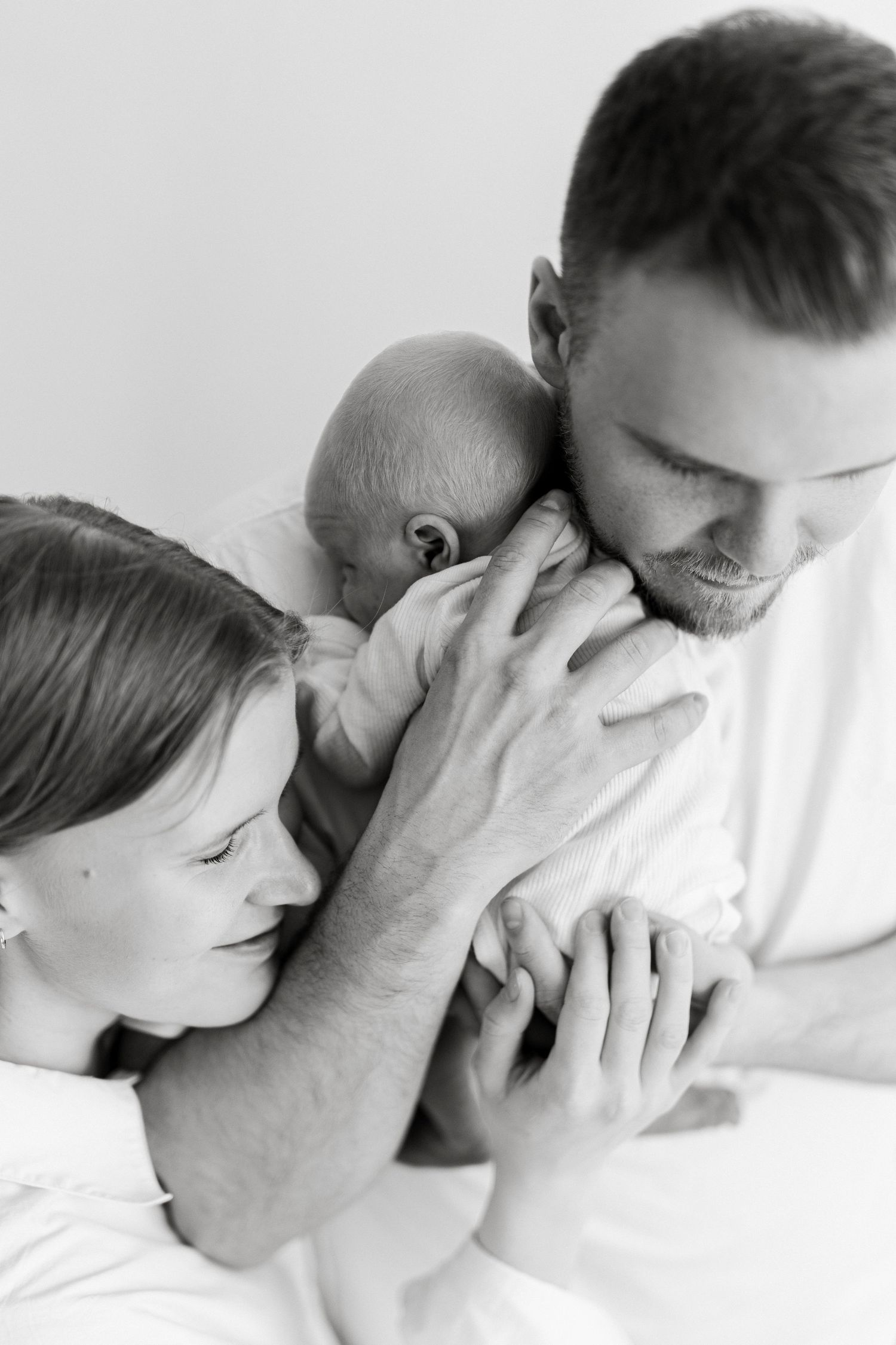 Black and white photo of parents tenderly holding and kissing their newborn baby together.