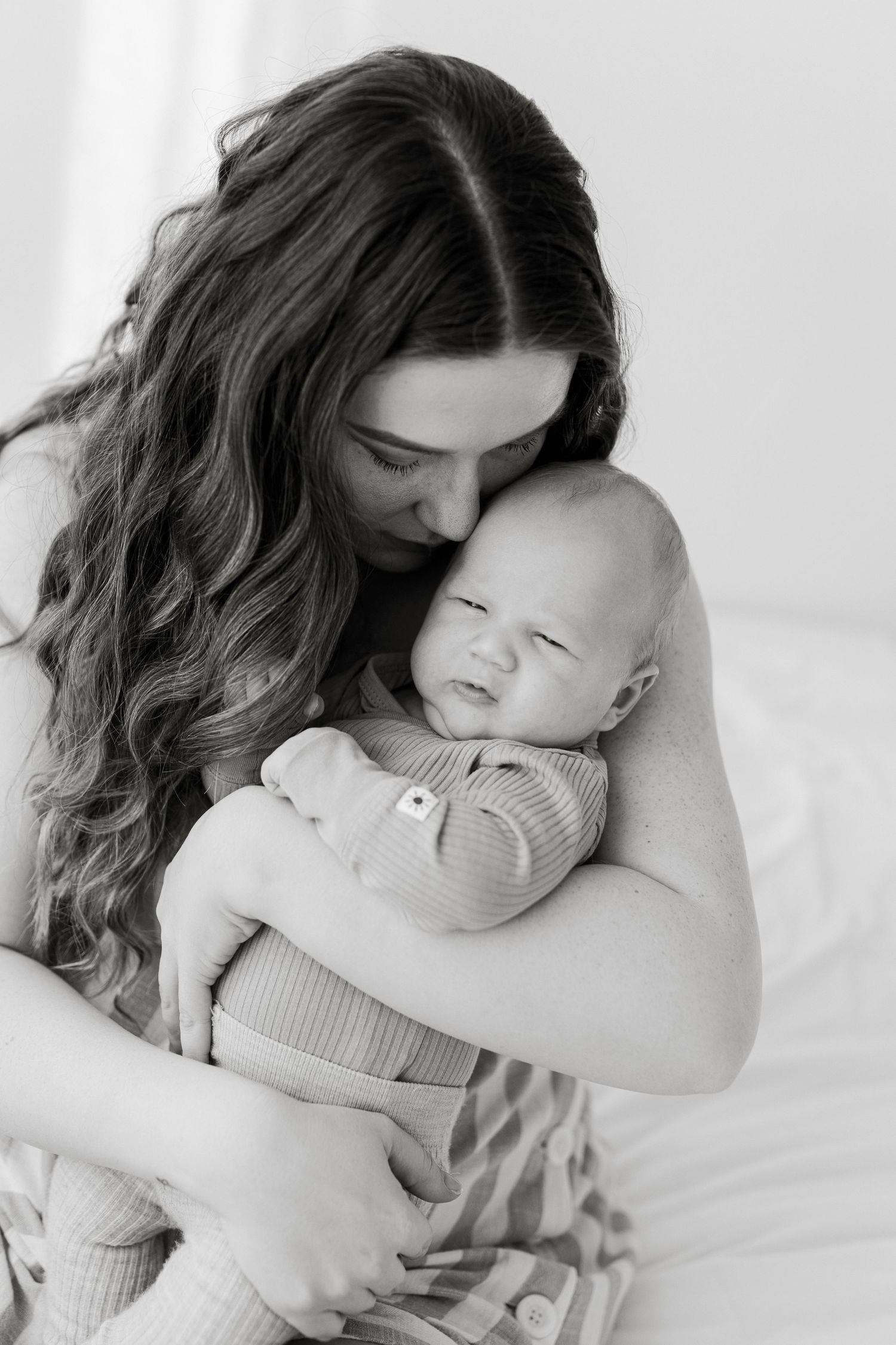 Black and white photo of a mother with long wavy hair tenderly holding and nuzzling her newborn baby.