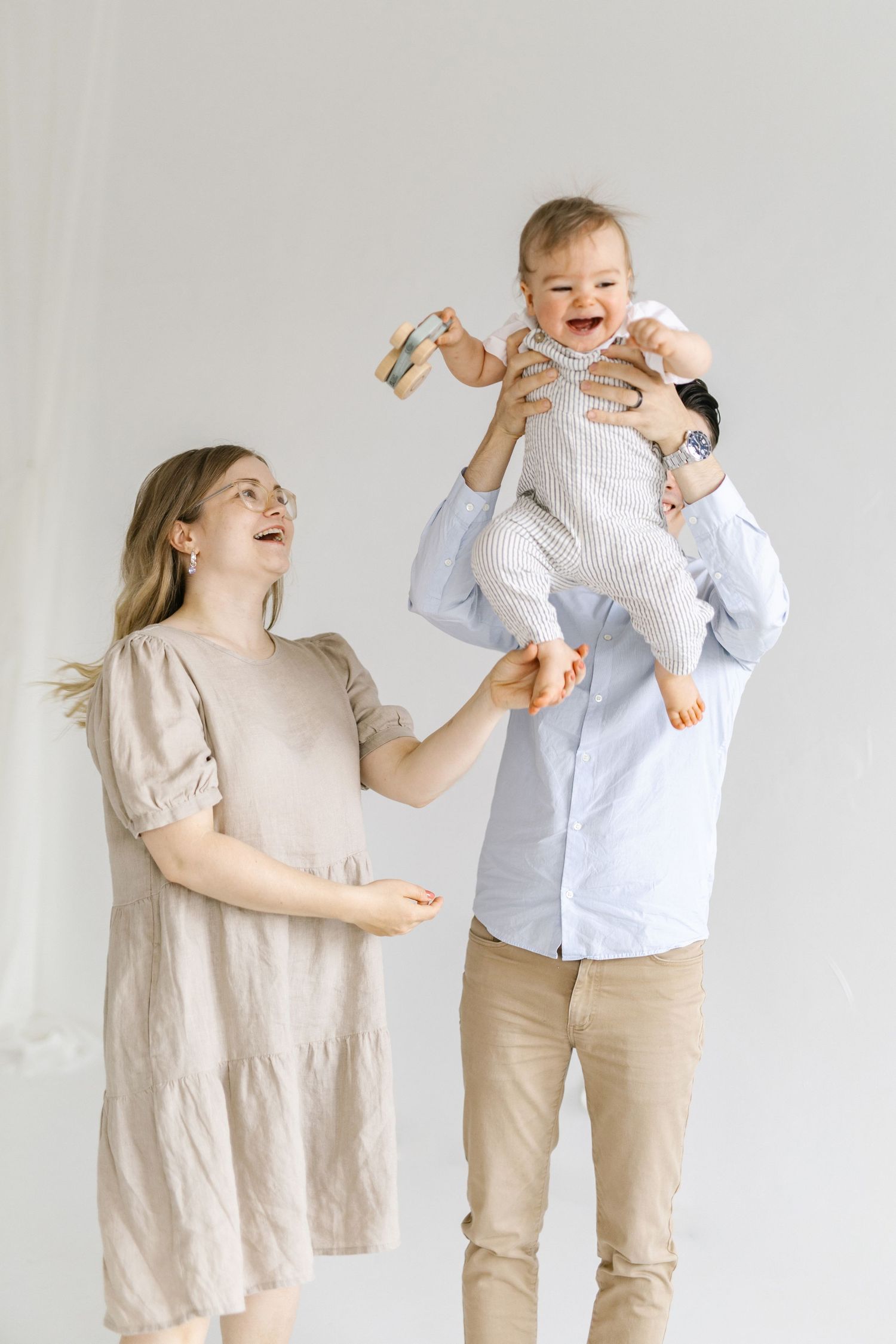 Happy family playing and lifting baby in air against white background.