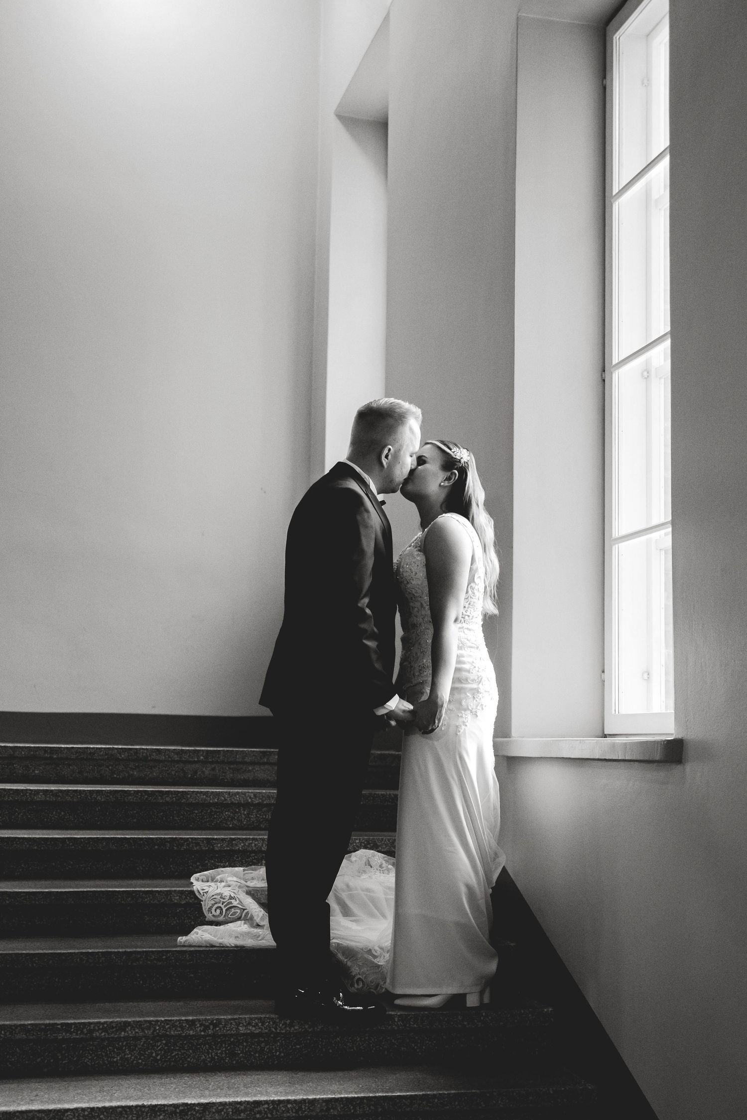 An intimate black and white wedding moment captured on a staircase by a window.