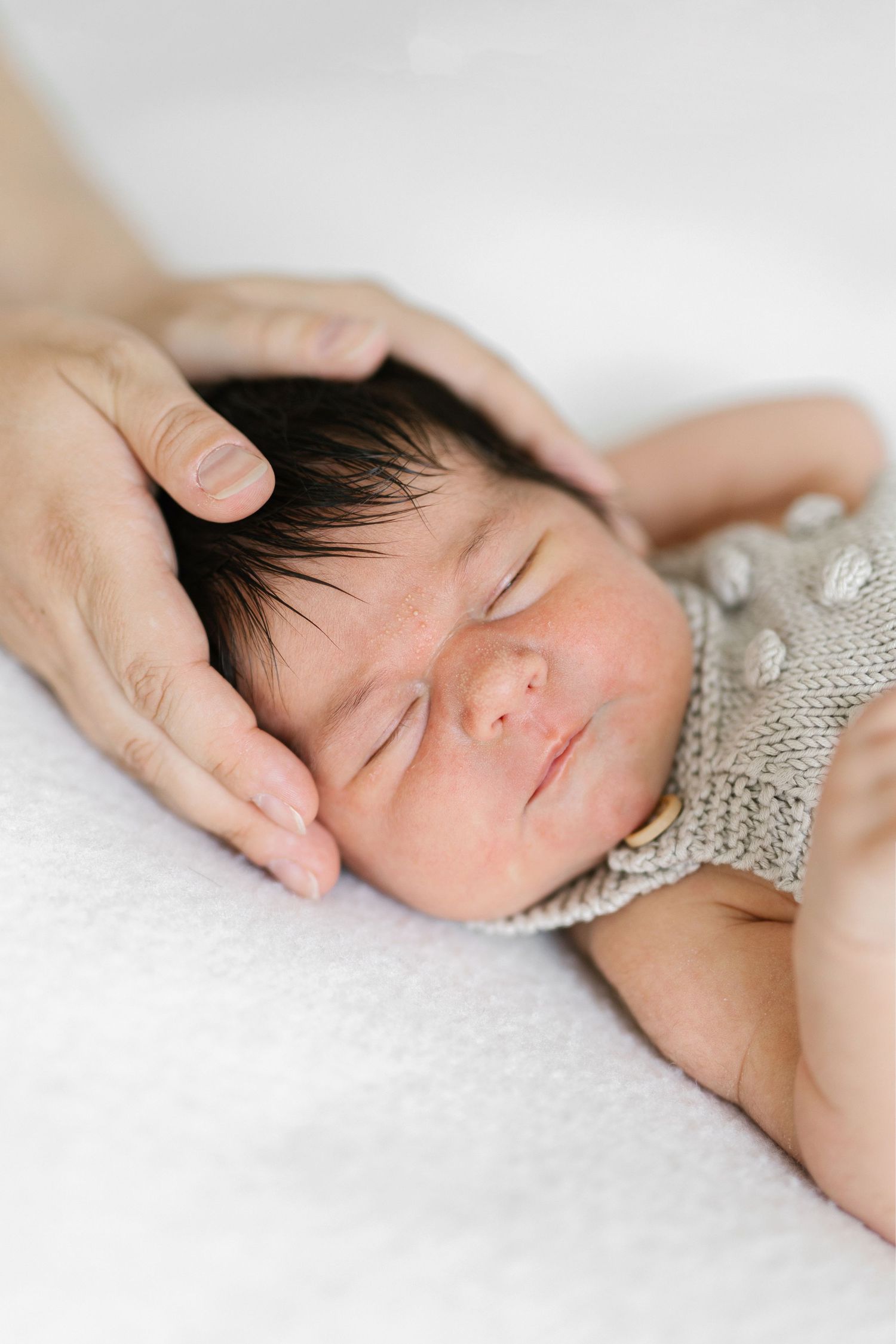 Sleeping newborn baby in knit bonnet cradled gently by parent's hand on white blanket.