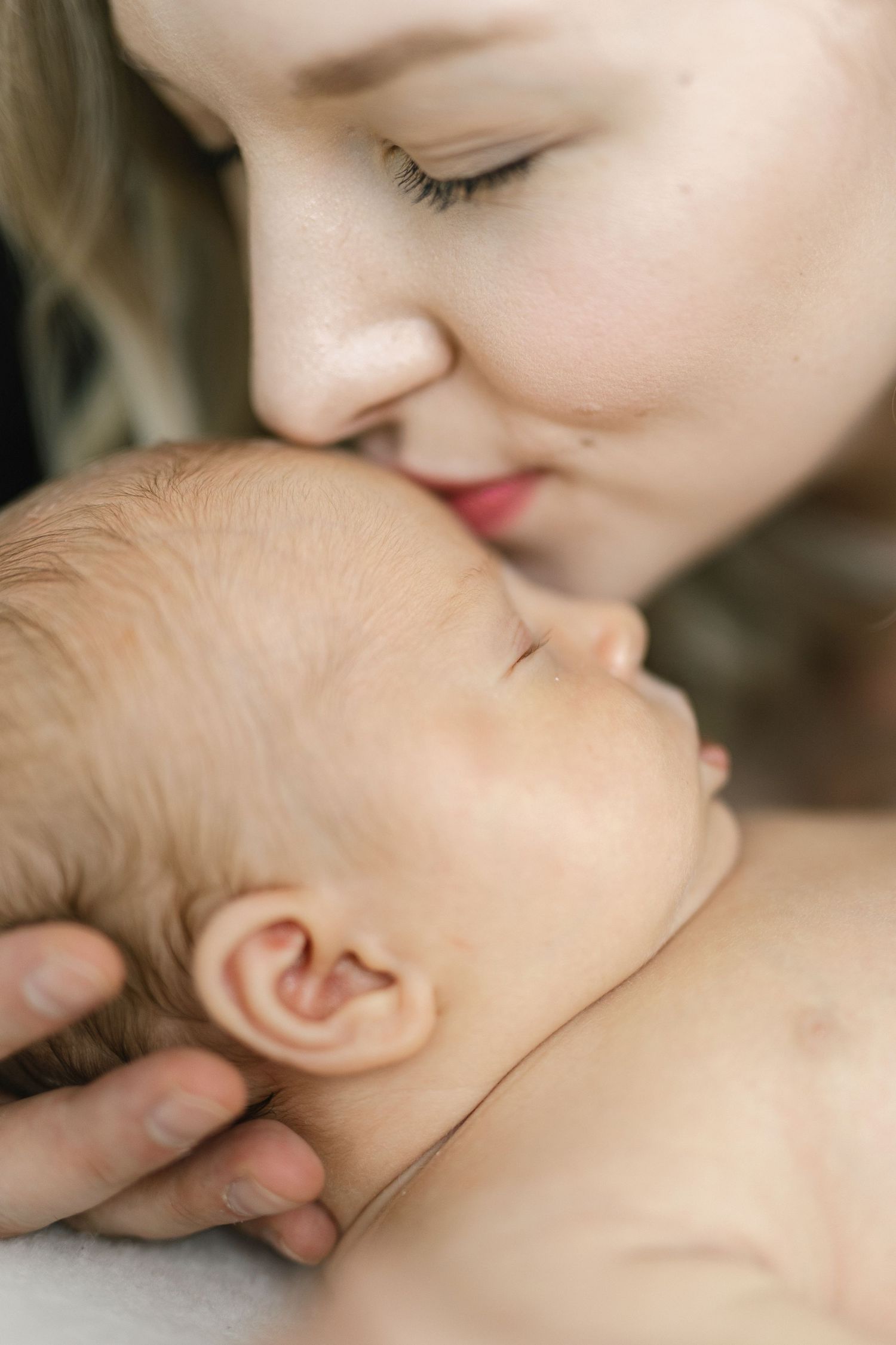 A tender moment as a mother gently kisses her sleeping newborn baby on the head.