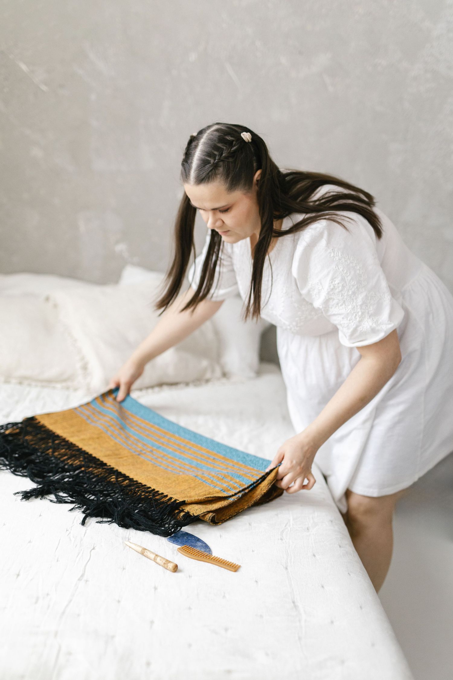 Person in white dress arranging textiles and fabrics on white surface.