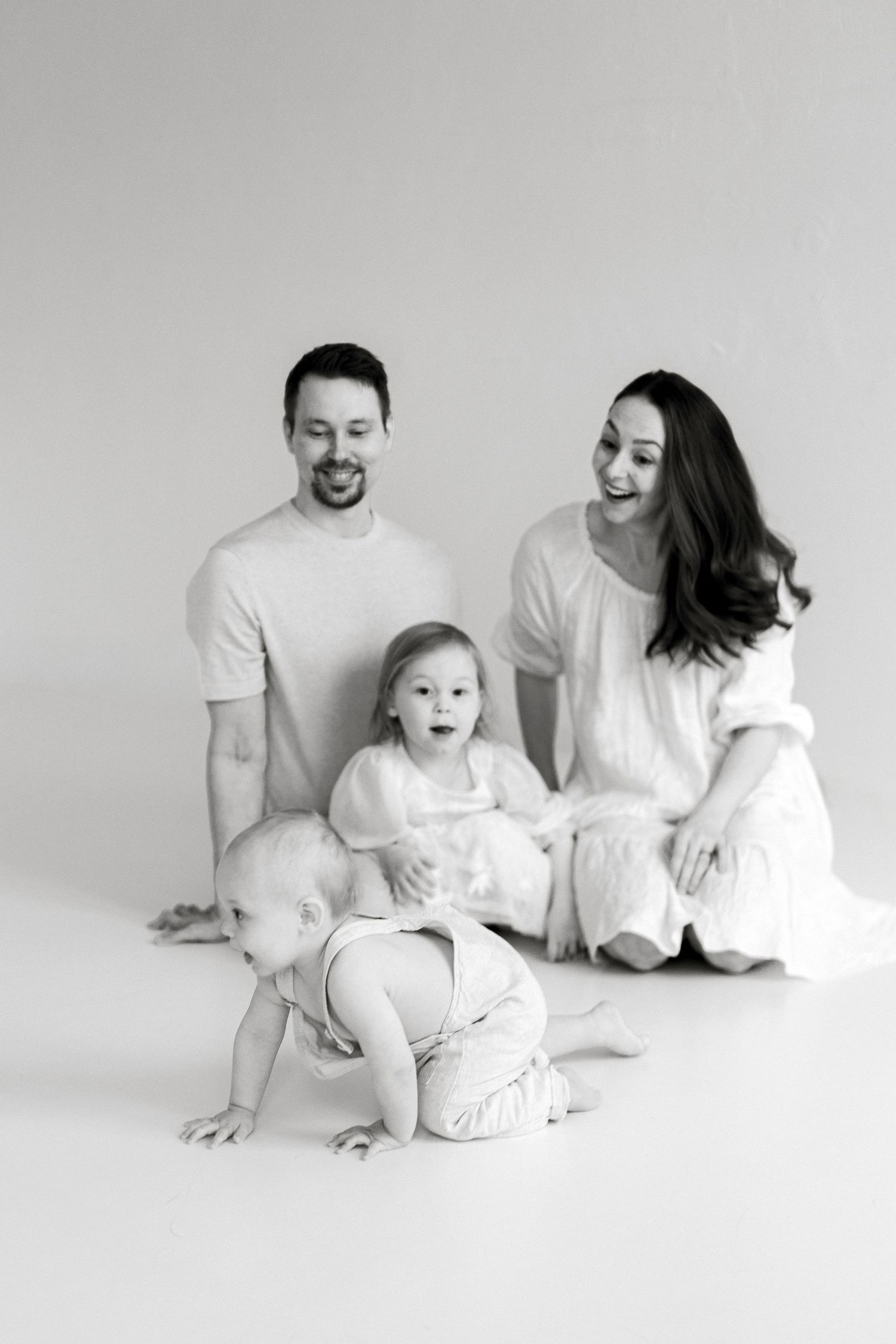 A minimalist black and white photo series showing a family sitting together on the floor in matching white outfits.