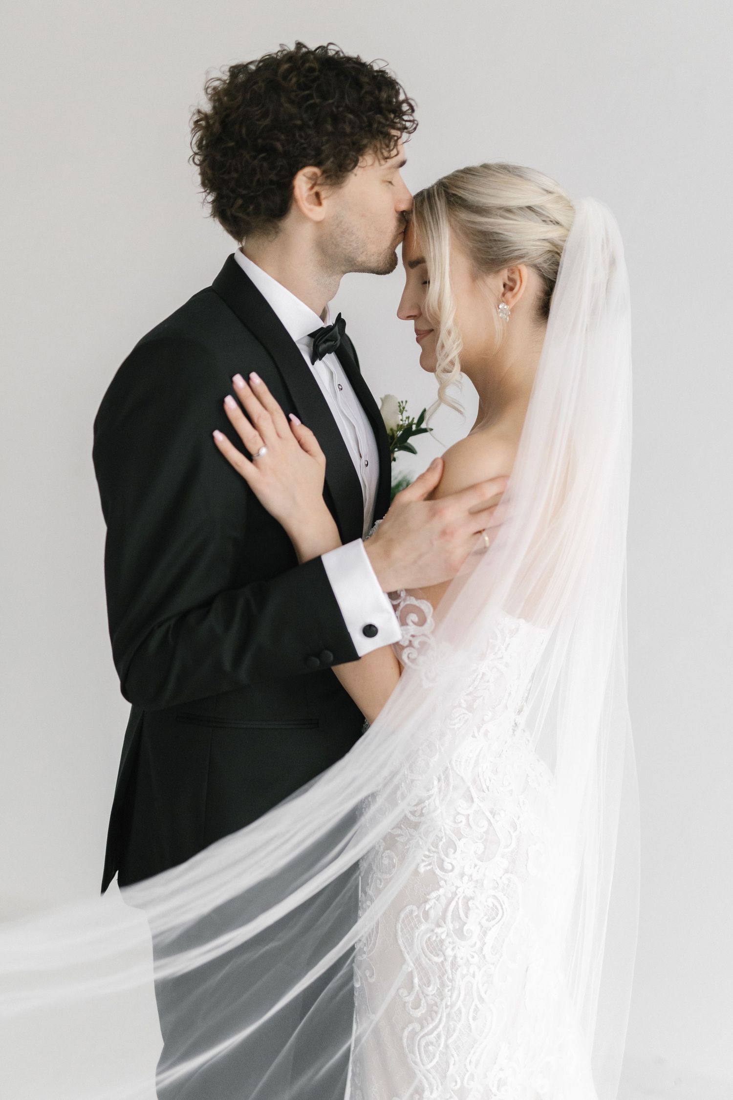 Romantic wedding portrait with flowing veil and classic black and white formal attire.
