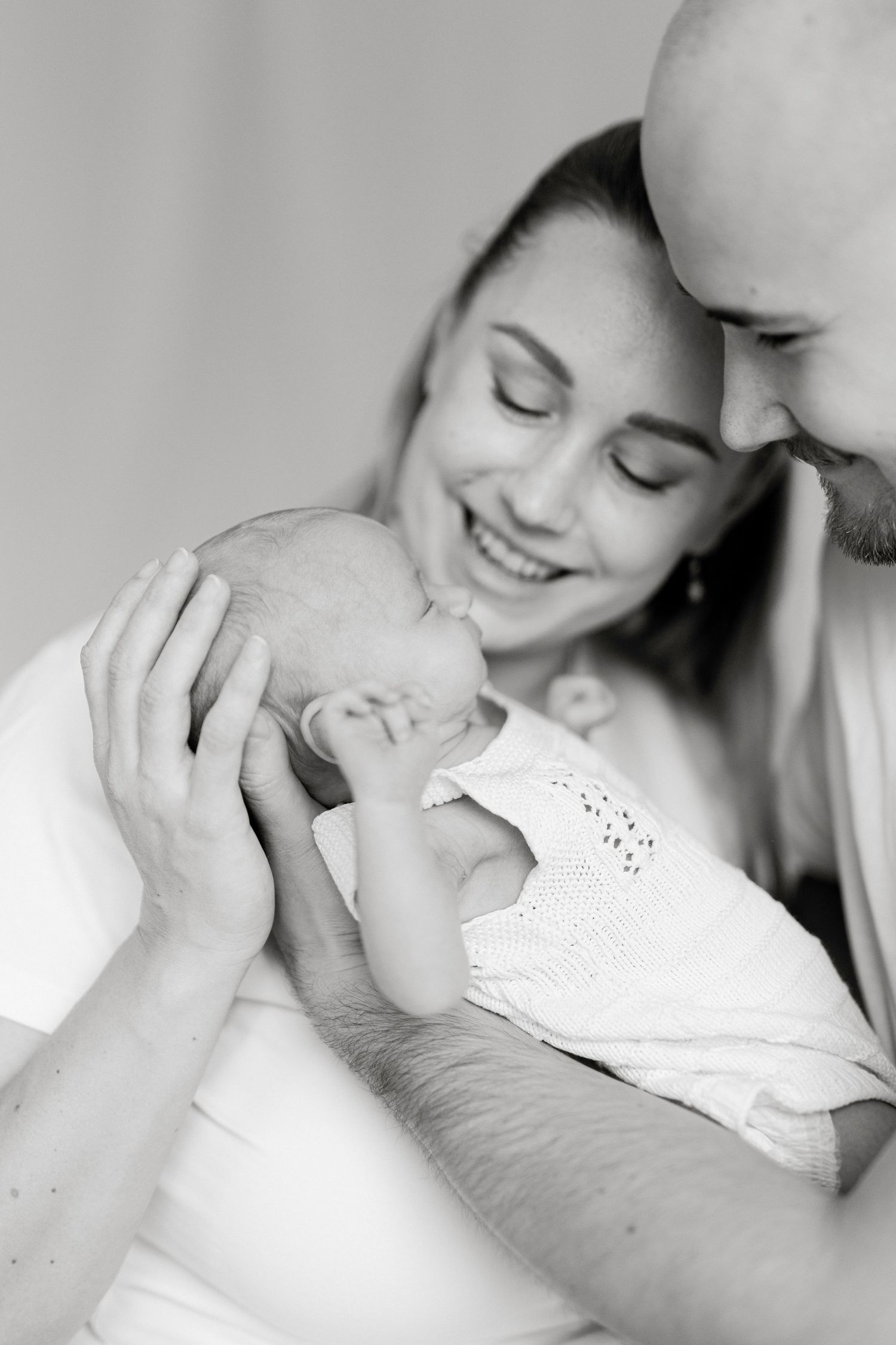 Intimate black and white portrait of parents sharing a tender moment with their sleeping newborn.