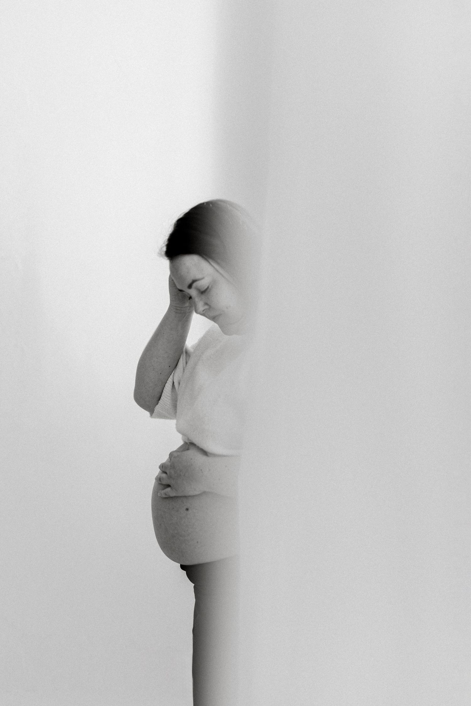 Artistic black and white portrait of expectant mother in profile against light background.