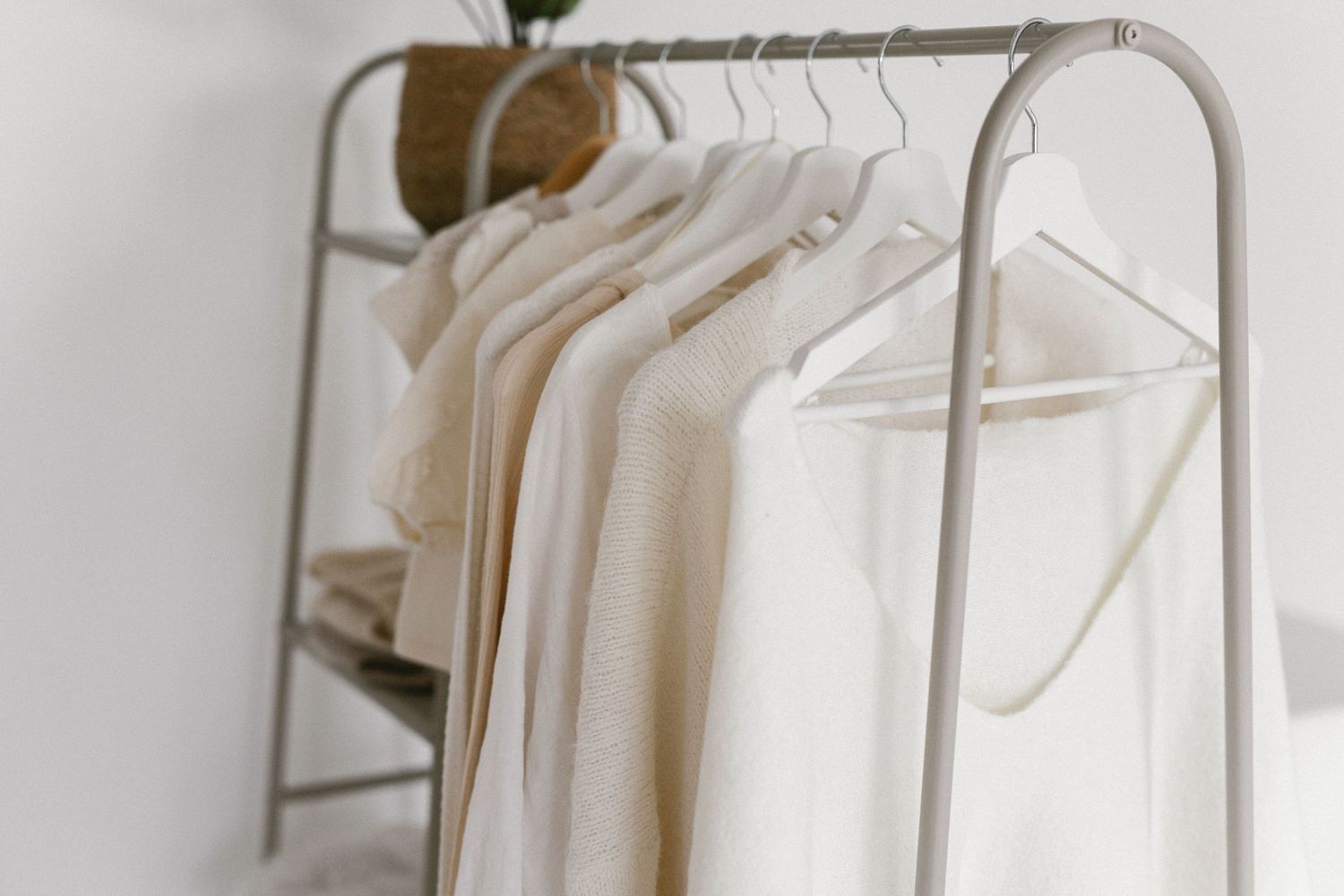 White and cream clothing items hanging neatly on a minimalist gray garment rack against a white wall.