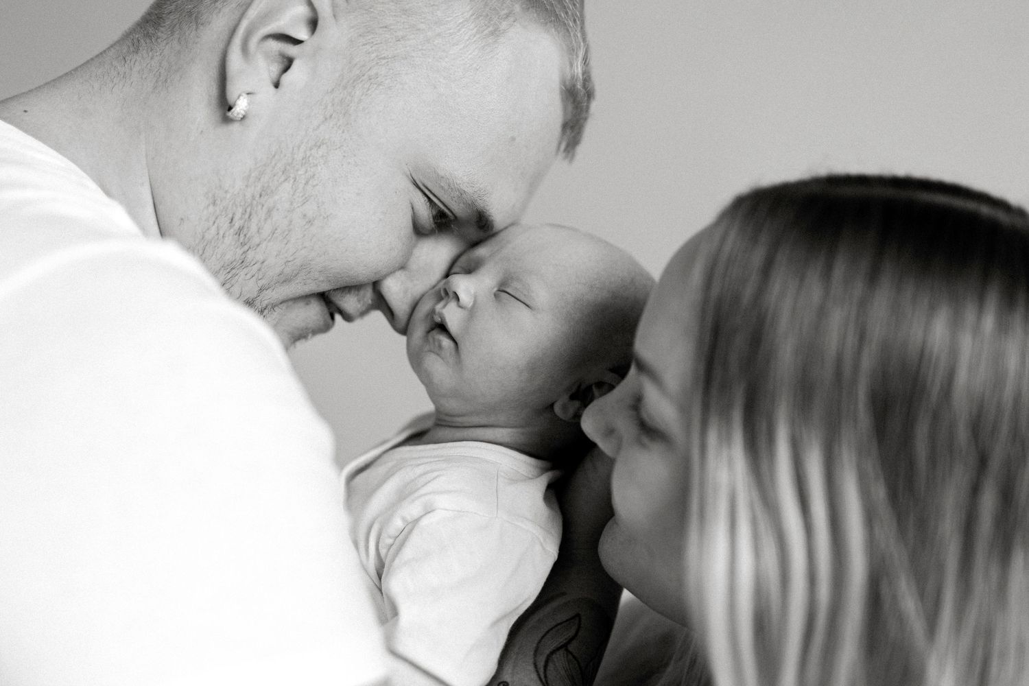 Black and white photo of parents lovingly holding and nuzzling their newborn baby together.