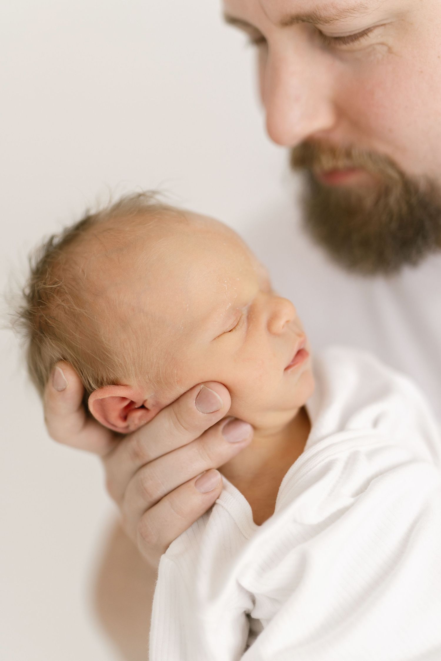 Close-up series showing gentle support of newborn baby's head against white background.