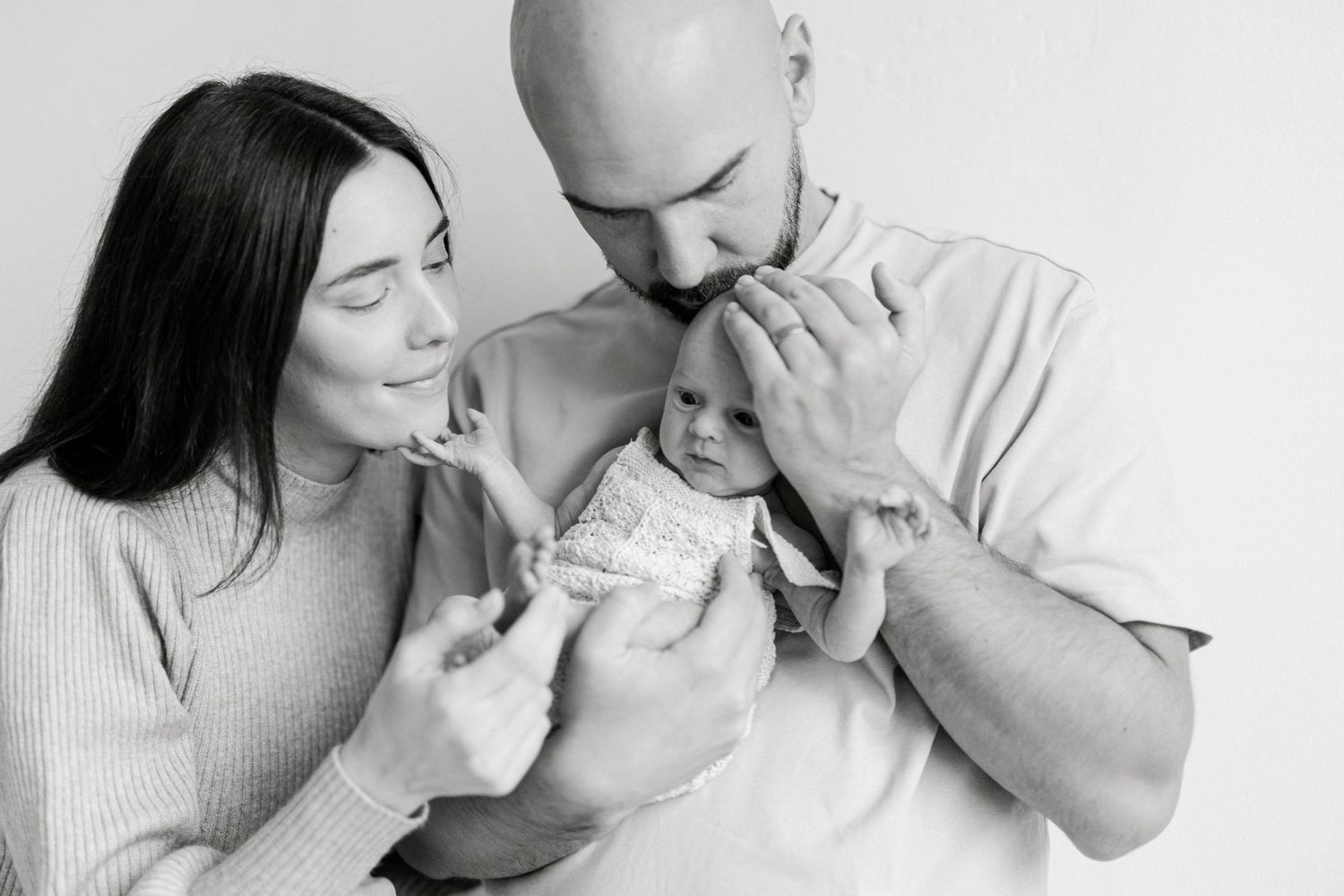 Black and white photo of new parents tenderly holding their newborn baby, sharing a precious family moment.