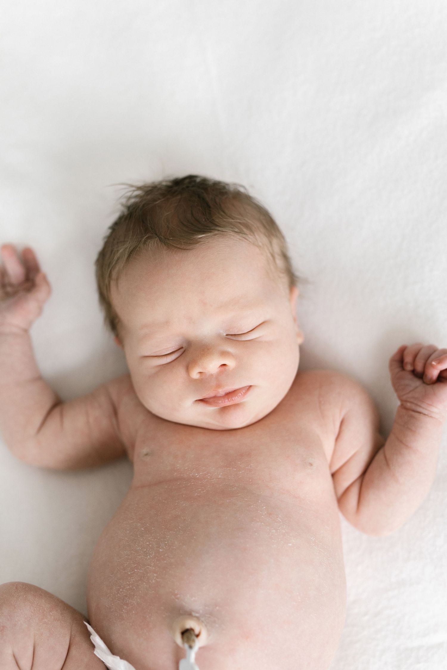 Peaceful newborn sleeping on white blanket in minimalist setting.