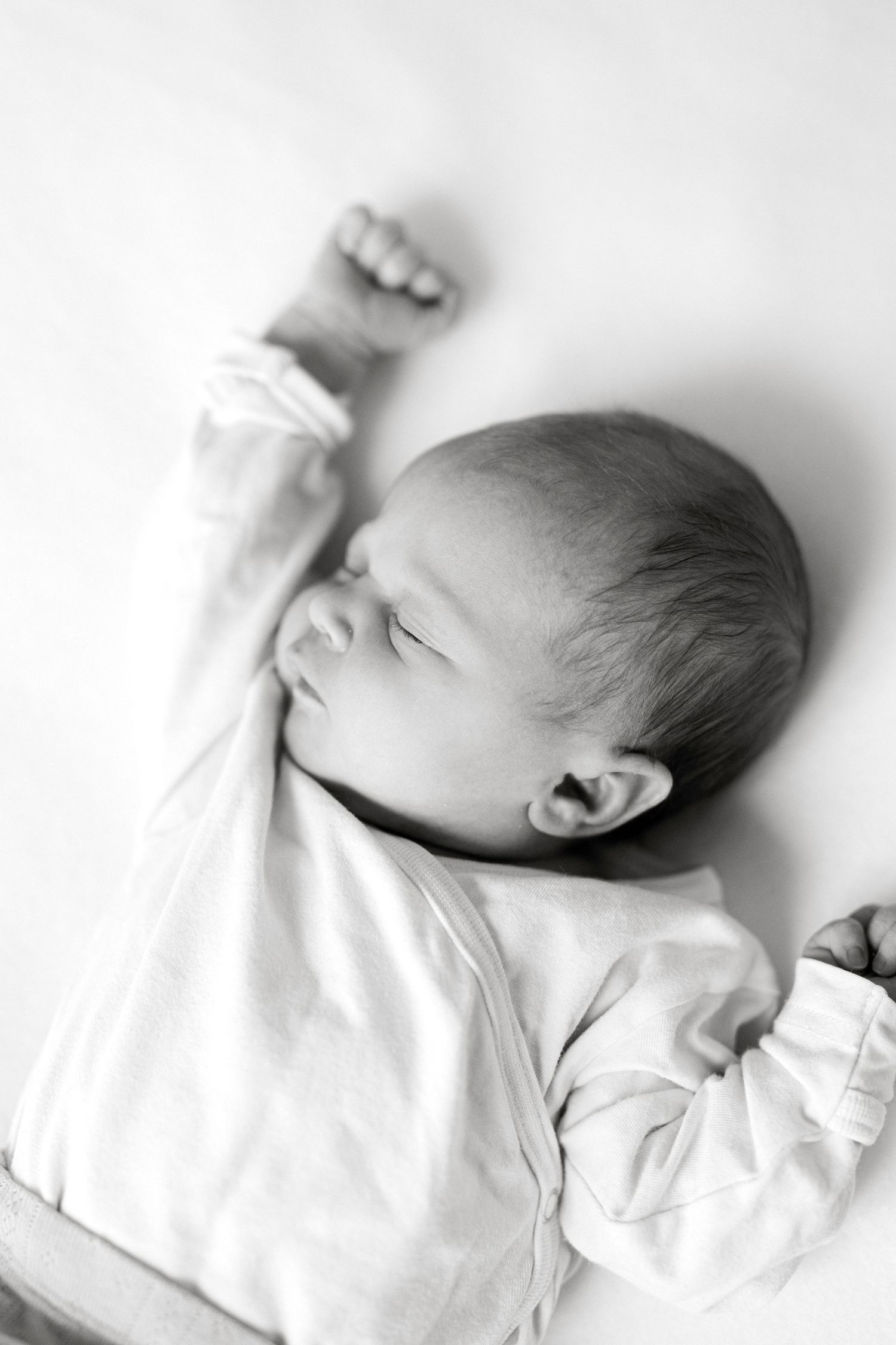 High-key portrait of a sleeping newborn in white clothing against a light background.