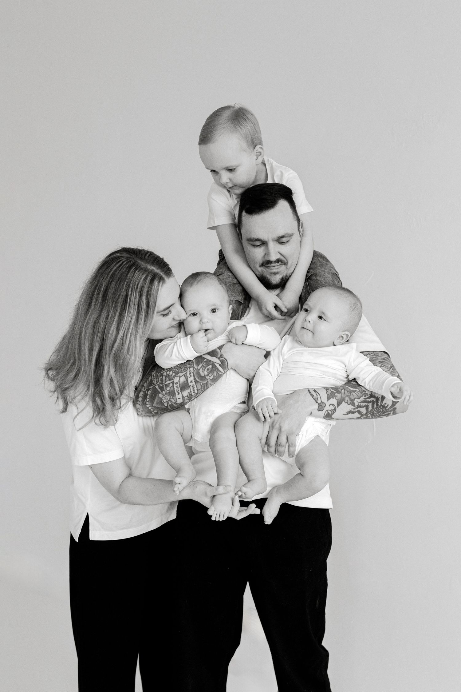 A family portrait showing parents holding multiple young children against a light background.