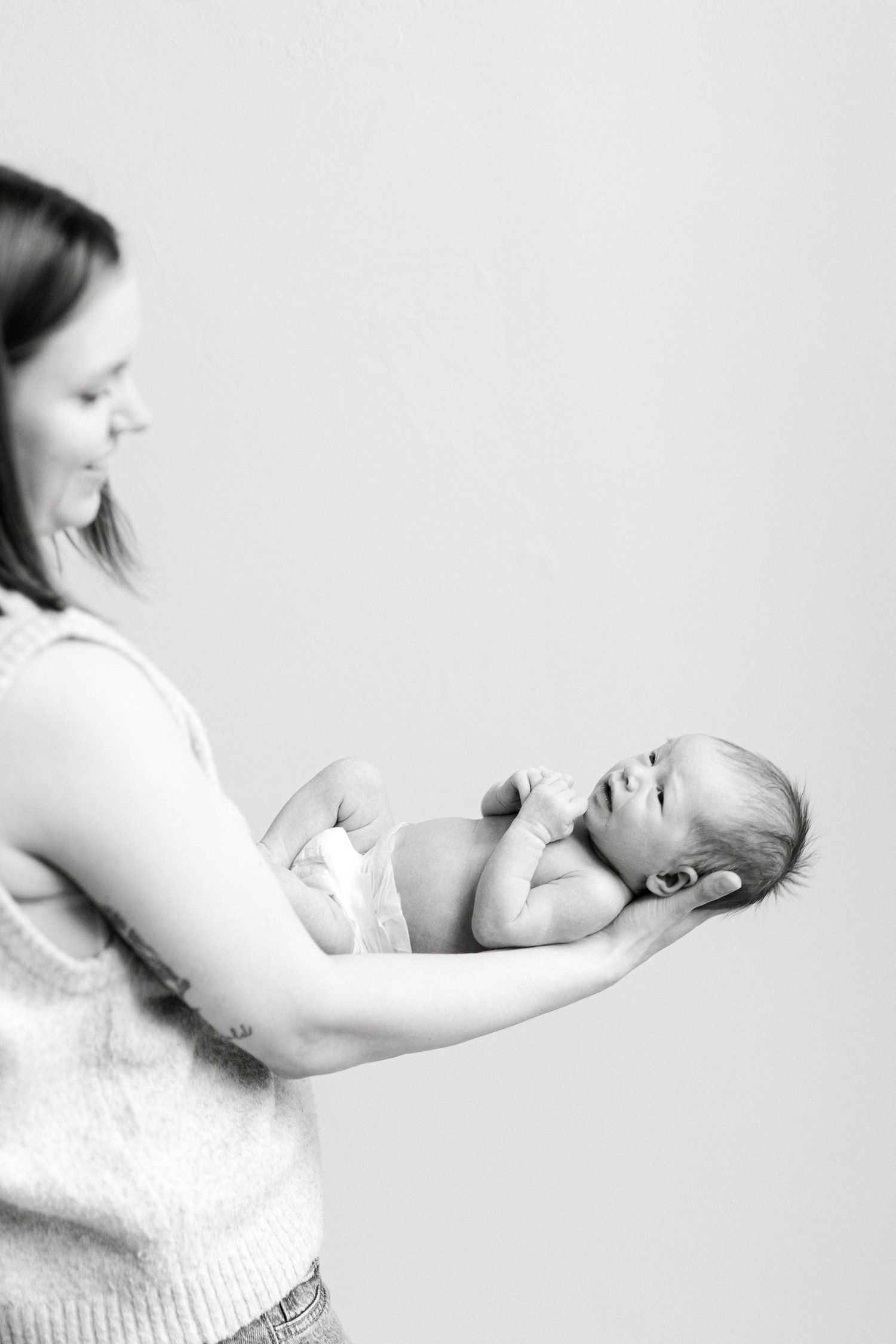 Black and white photo of a mother tenderly holding her newborn baby in her arms against a light background.