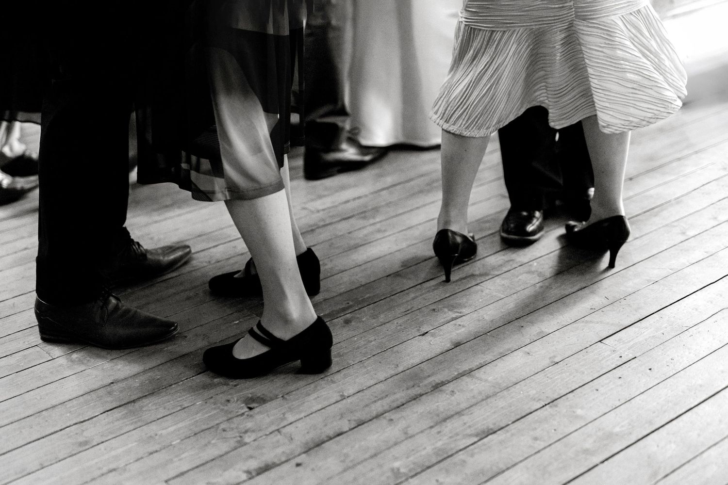 Black and white photo of couples dancing on wooden floor, showing elegant heels and dress shoes.