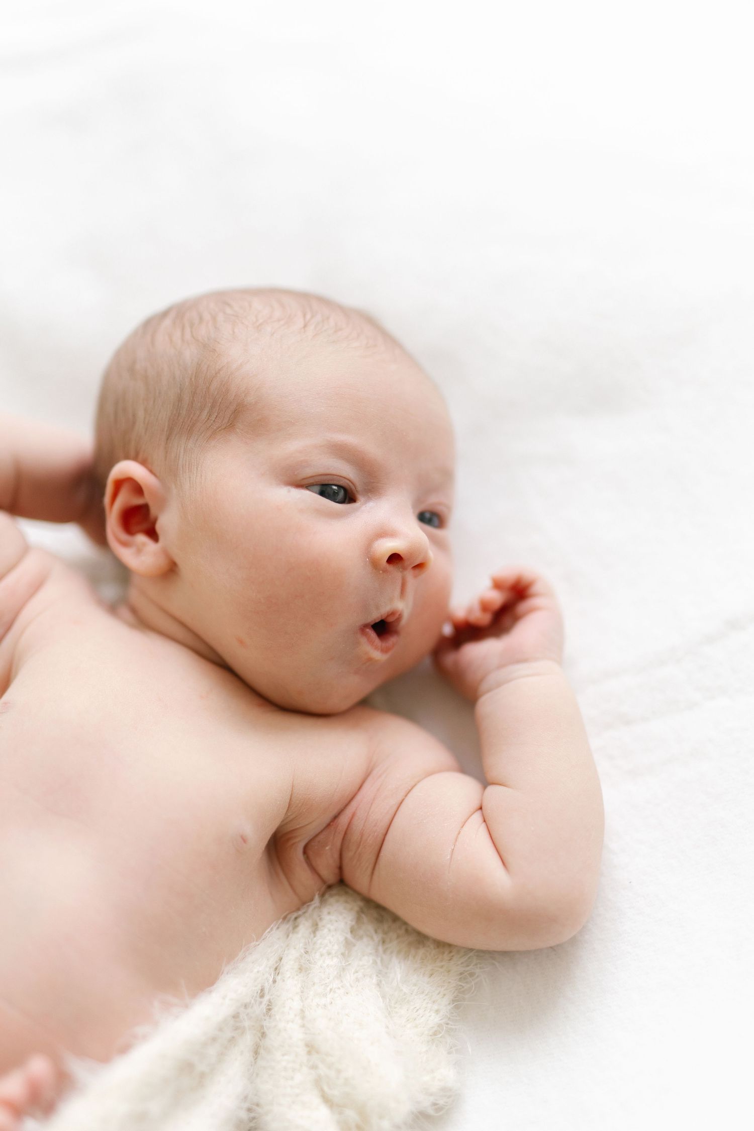 Newborn baby stretching while lying on cream-colored blanket.