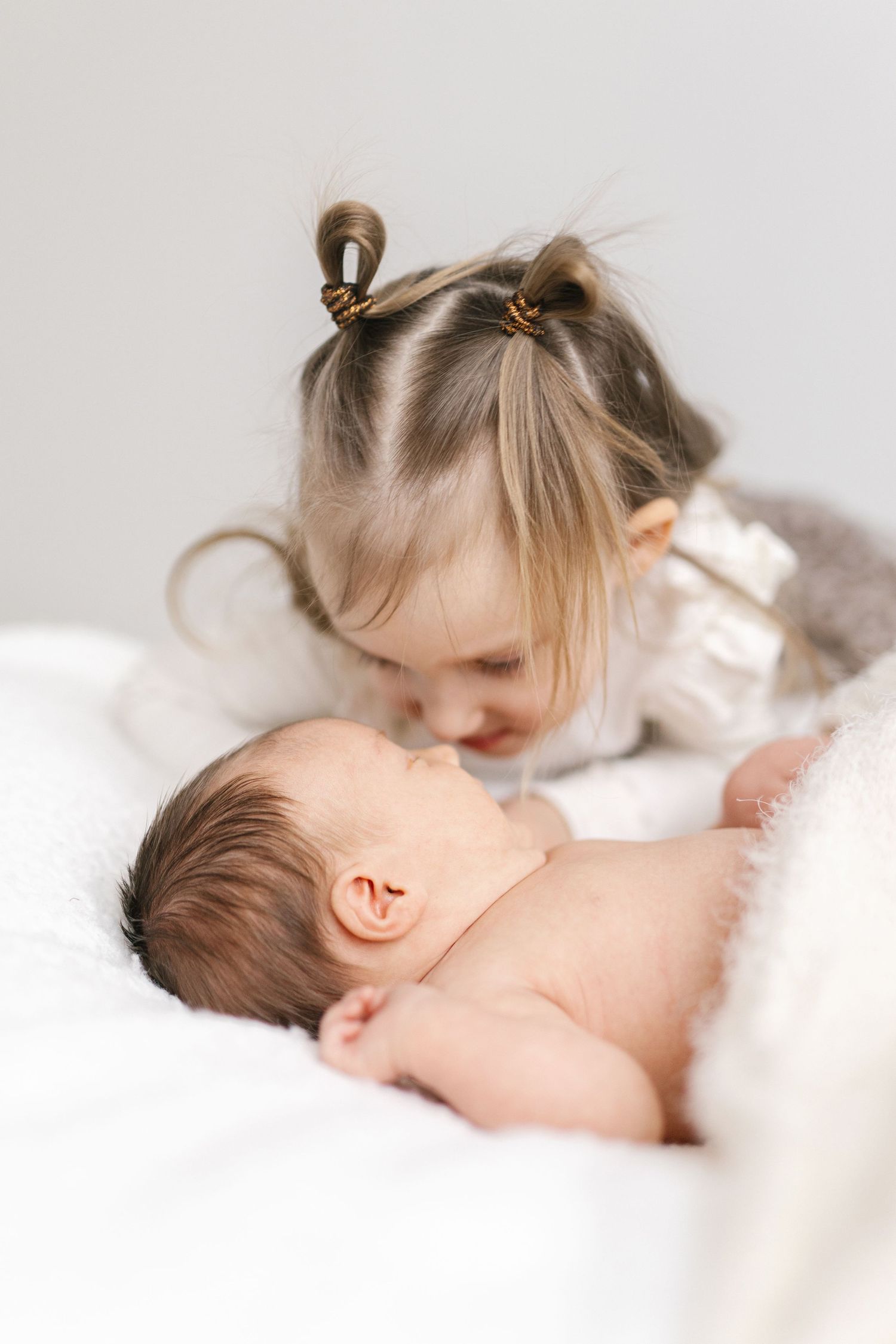 Intimate moment between siblings as toddler leans over sleeping newborn.