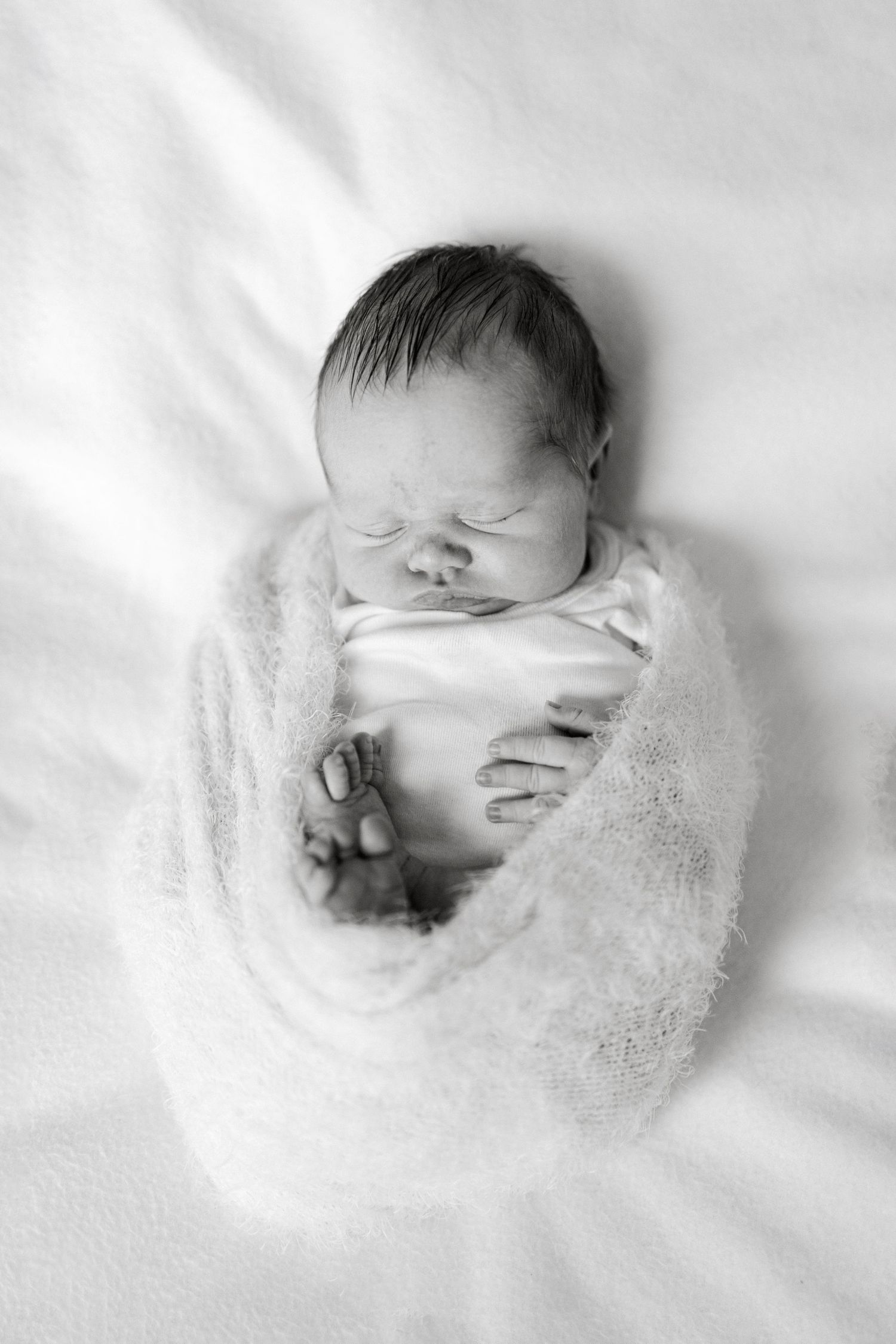 Black and white portrait of sleeping newborn swaddled in delicate lace wrap.