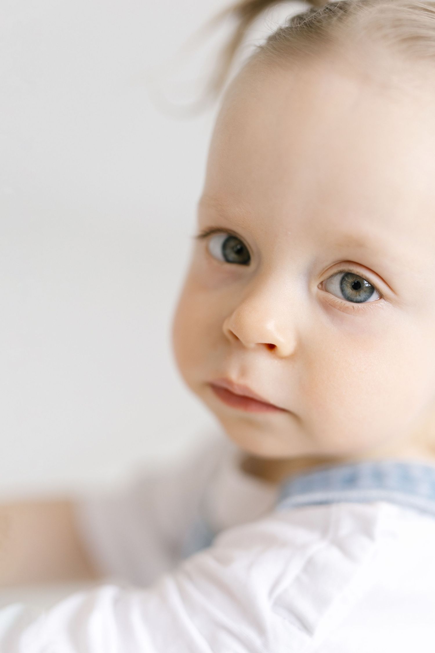Close-up portrait of a cute baby with blue eyes and fair skin wearing a white outfit.