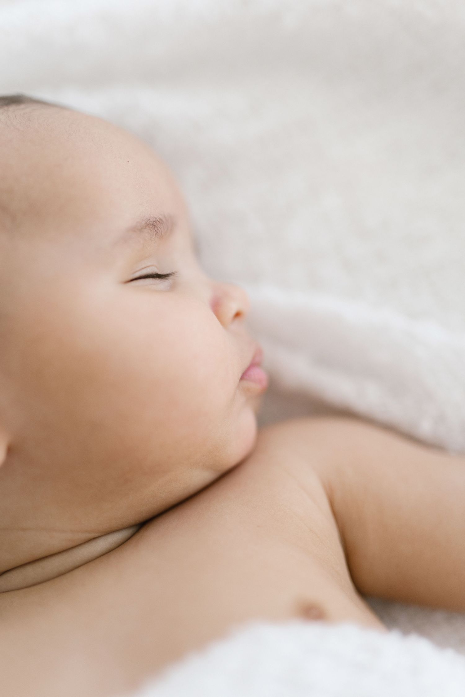 A peaceful newborn baby sleeping on a soft white blanket, with eyes closed and lips slightly parted.
