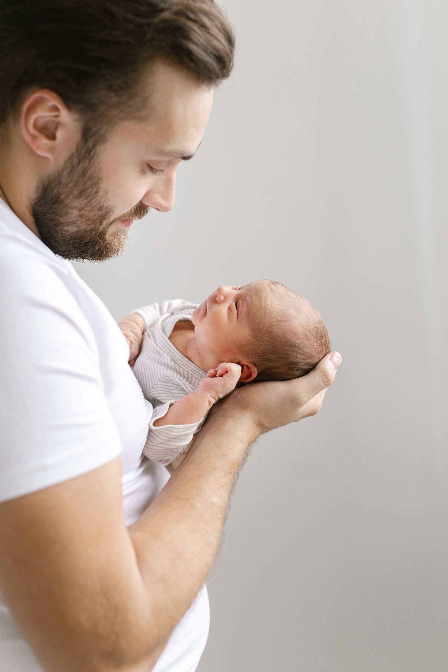 Parent holding and kissing newborn baby against light background.