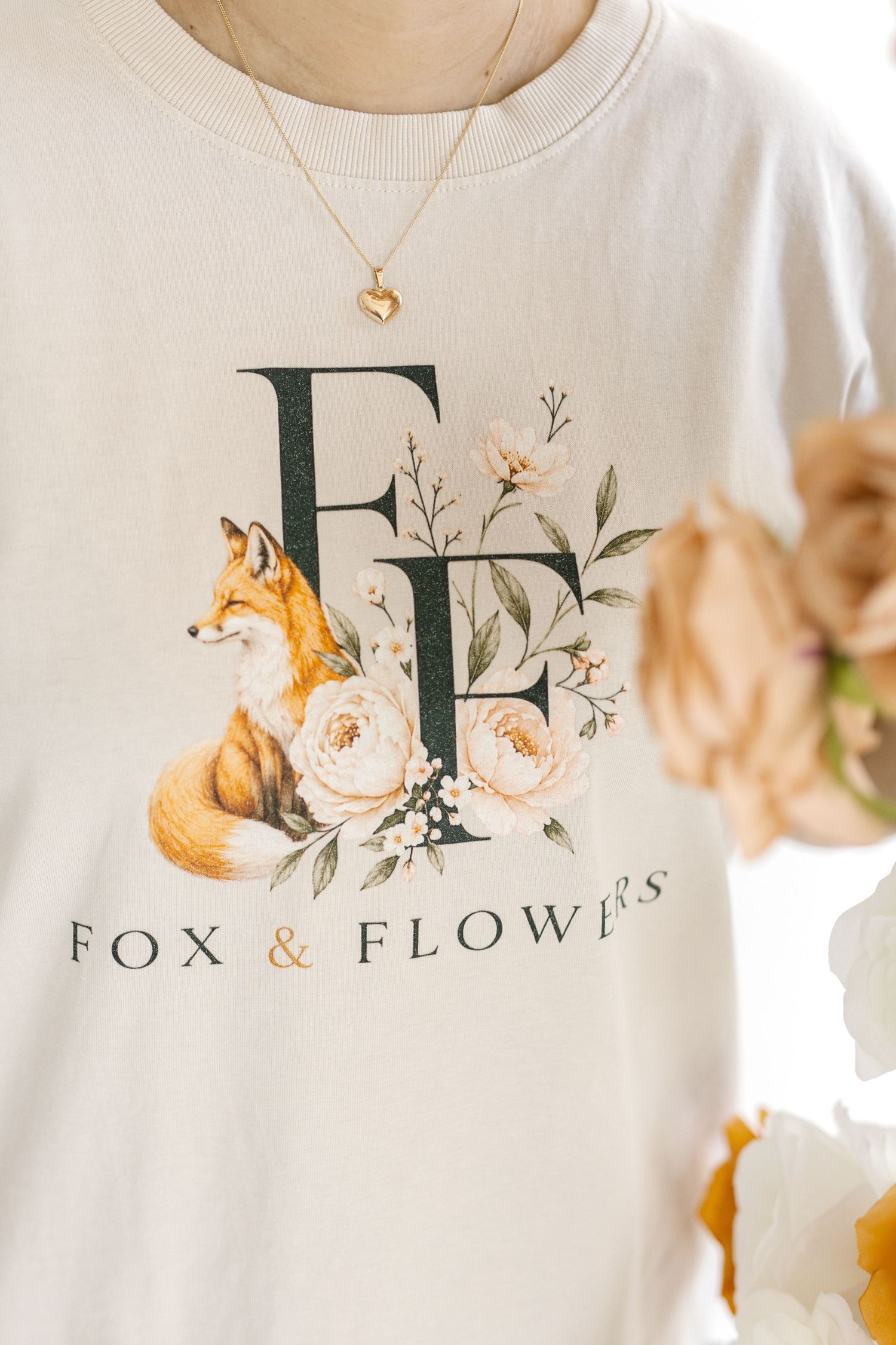 White sweatshirt with Fox & Flowers logo featuring a fox and floral design, worn with a gold heart necklace.