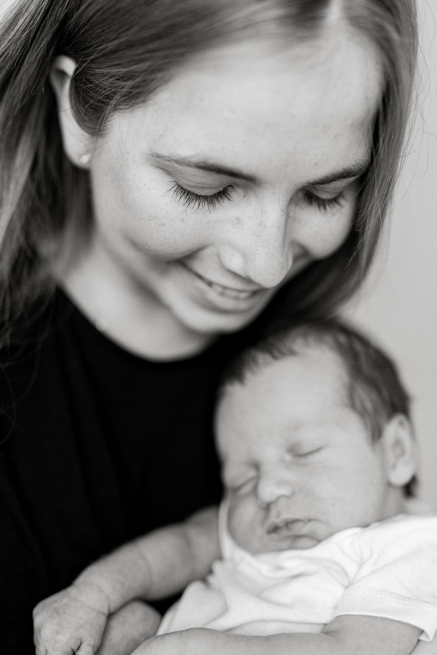 Black and white photo of a smiling young mother tenderly holding her sleeping newborn baby wrapped in white.