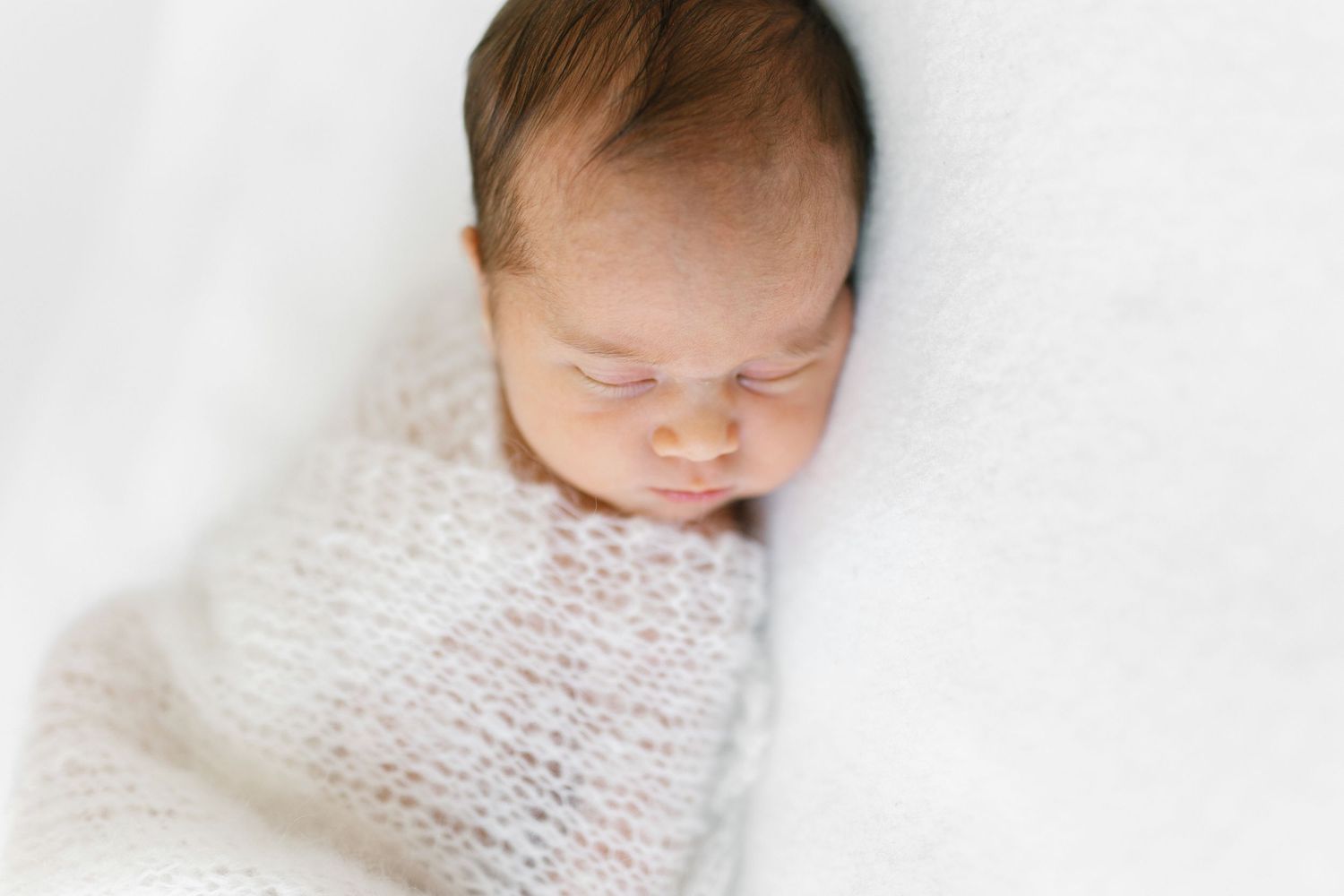 Sleeping newborn baby wrapped in soft white knitted blanket shown from multiple angles in gentle lighting.