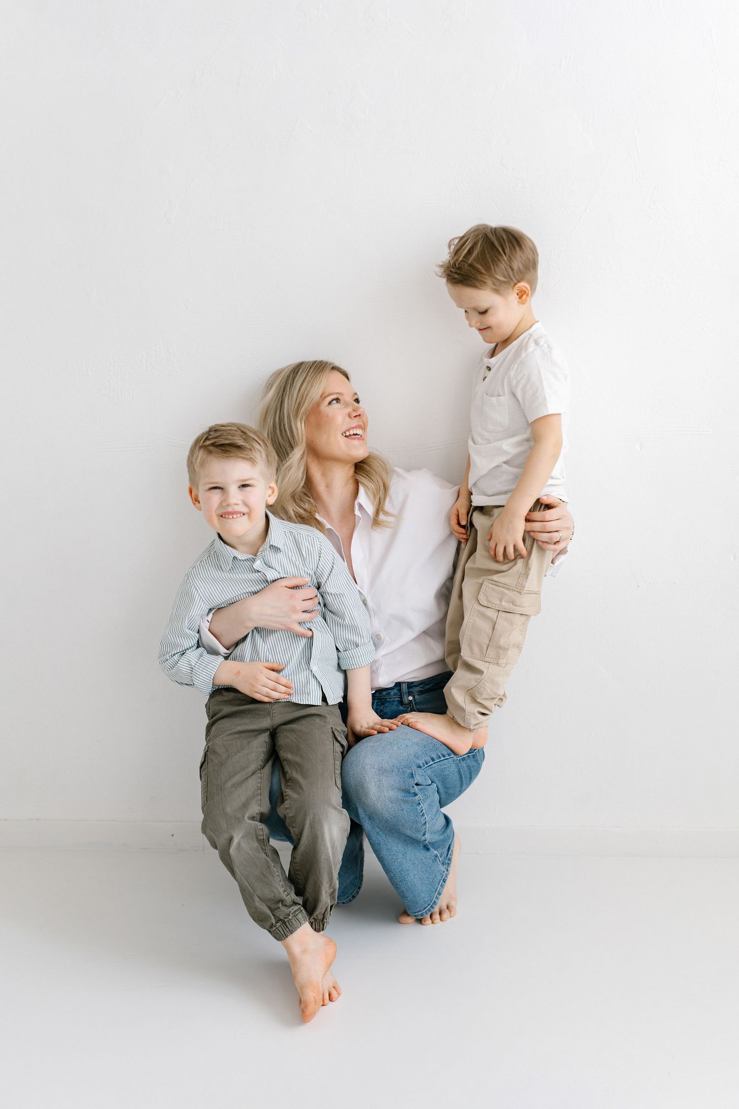 A minimalist white studio photo series showing tender family moments between a parent and children.