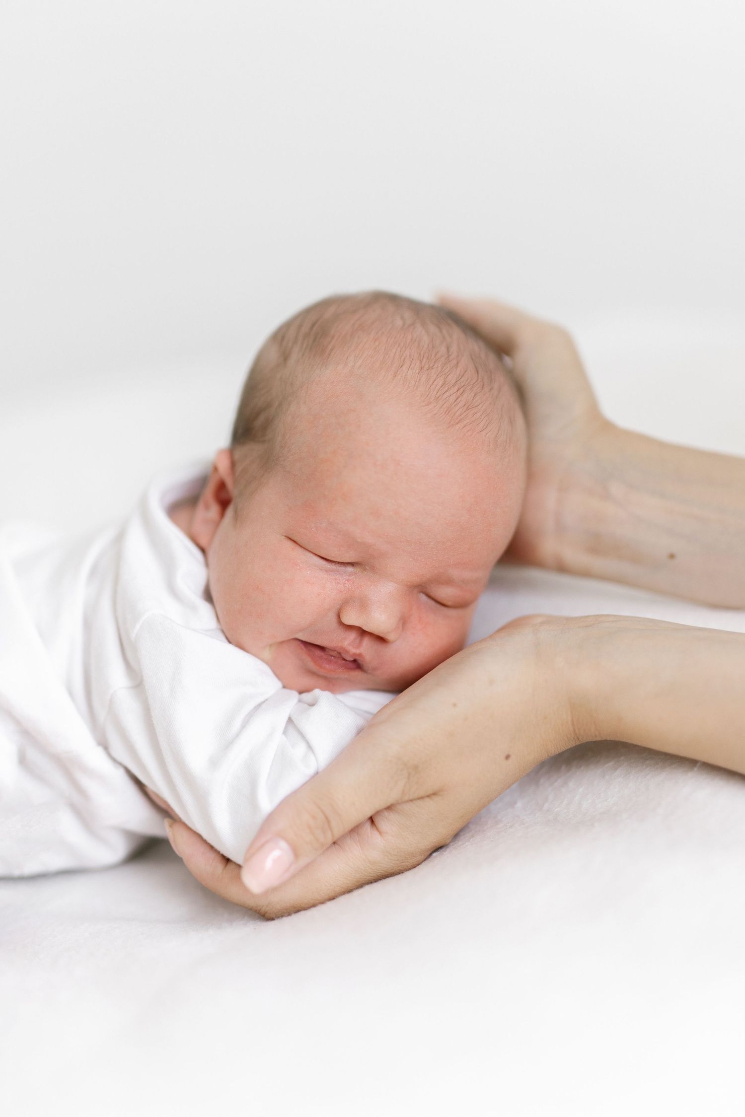 Gentle hands cradling sleeping newborn on white background in artistic portrait.